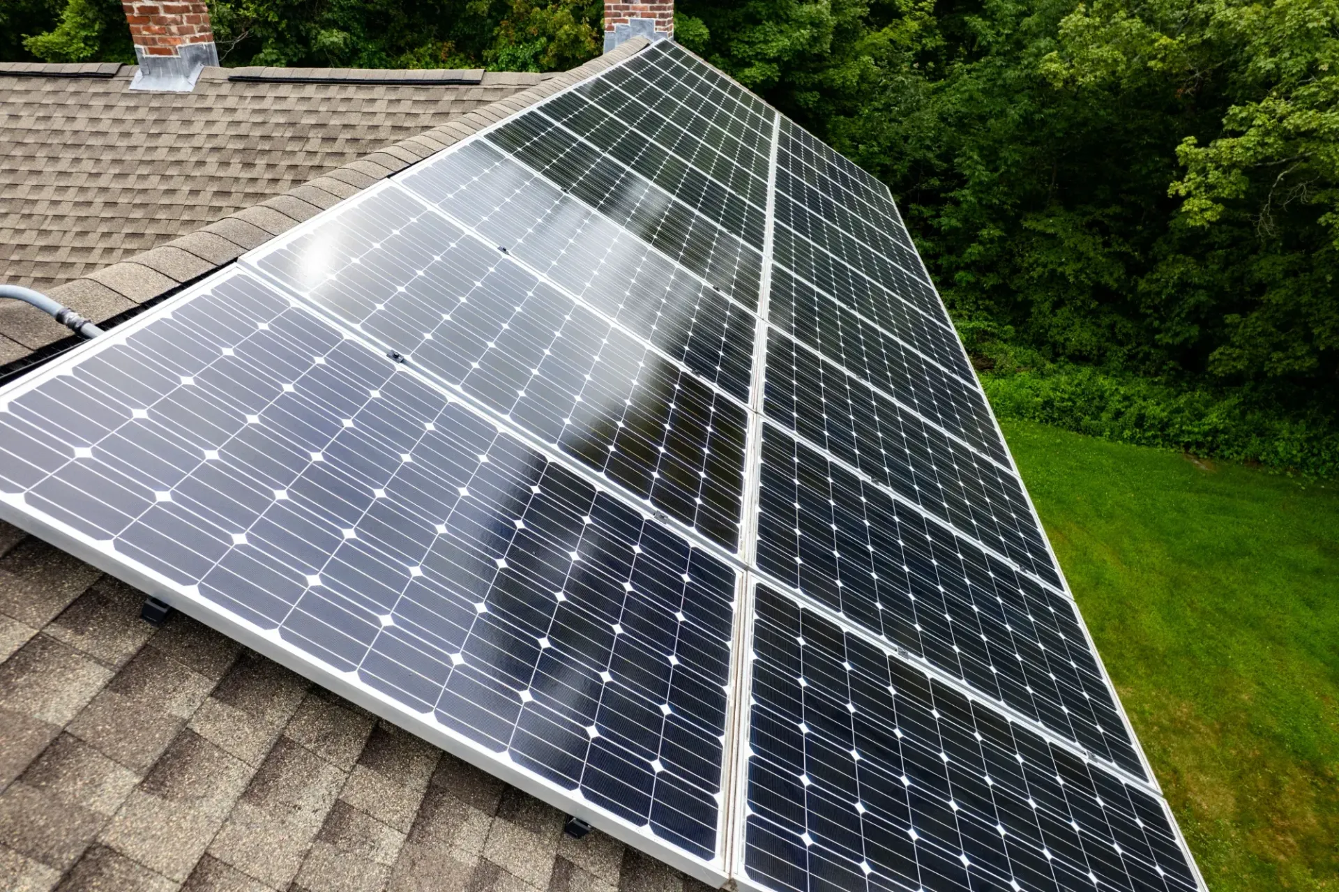 Solar panels installed on a sloped rooftop beside green trees and lawn. — Macleay Energy Solutions In Kempsey, NSW