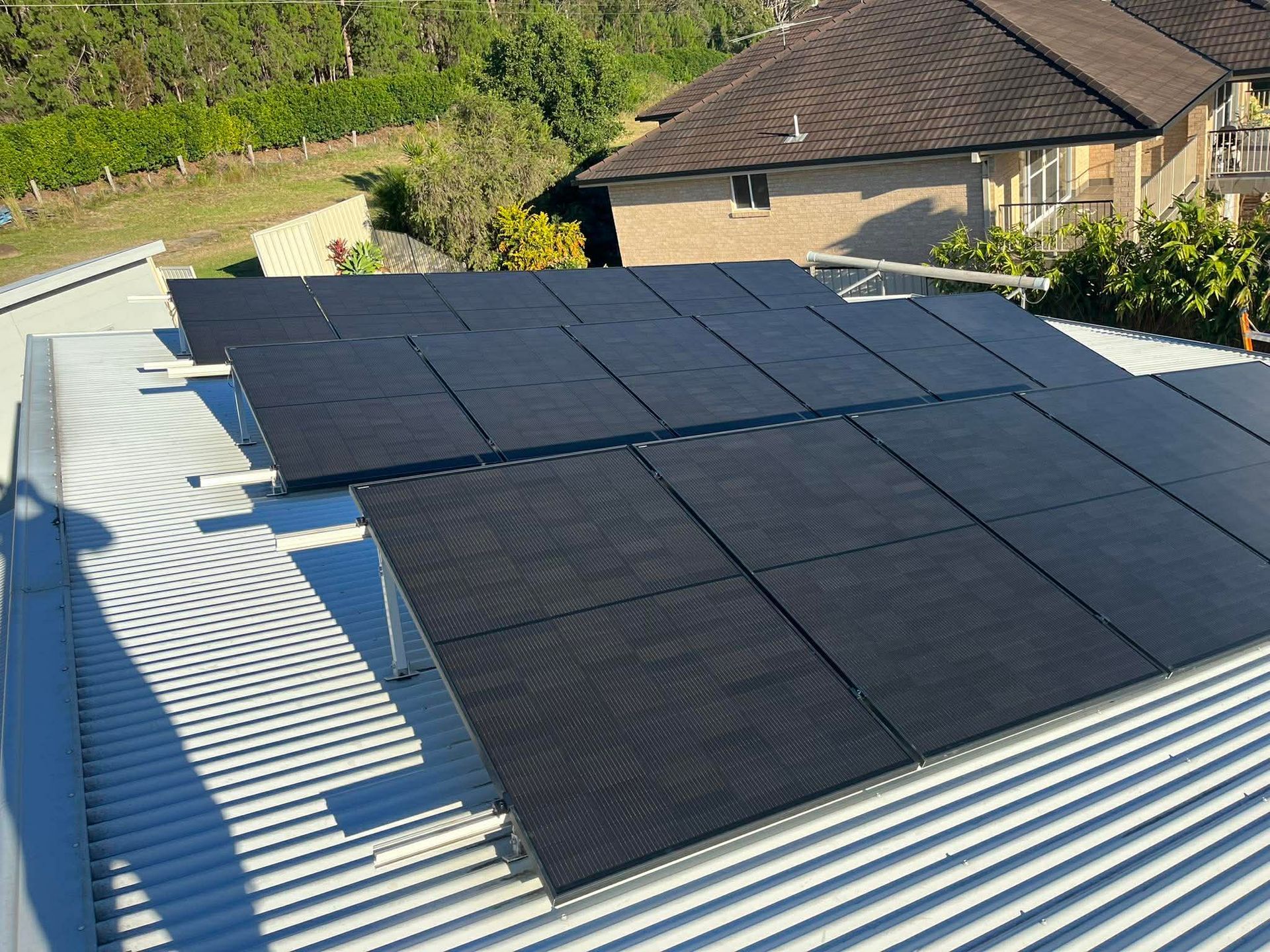 Solar panels installed on a corrugated roof beside a house and trees — Macleay Energy Solutions In Crescent Head, NSW