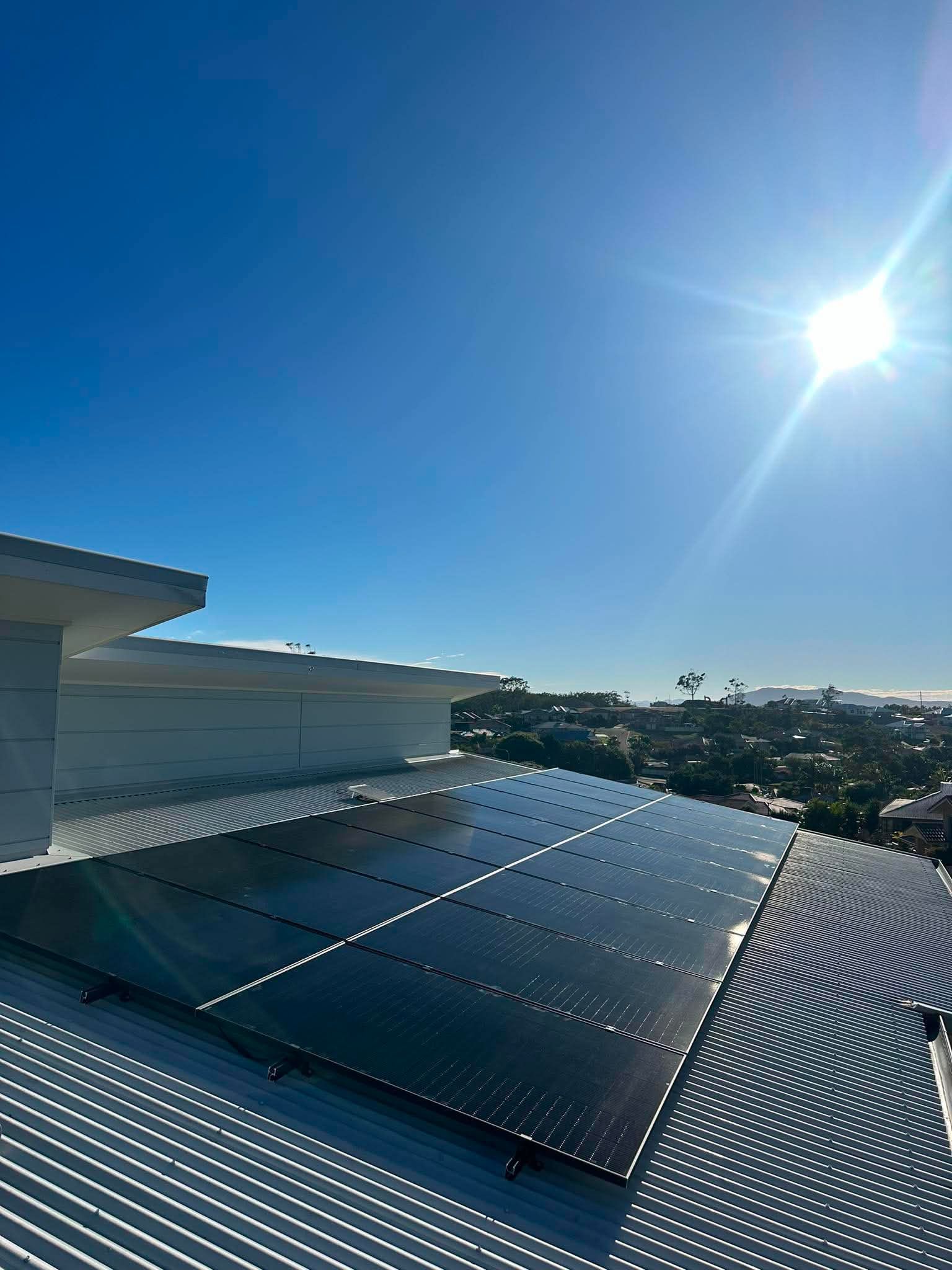 Solar panels on a corrugated rooftop under a bright blue sky with the sun shining — Macleay Energy Solutions In Crescent Head, NSW