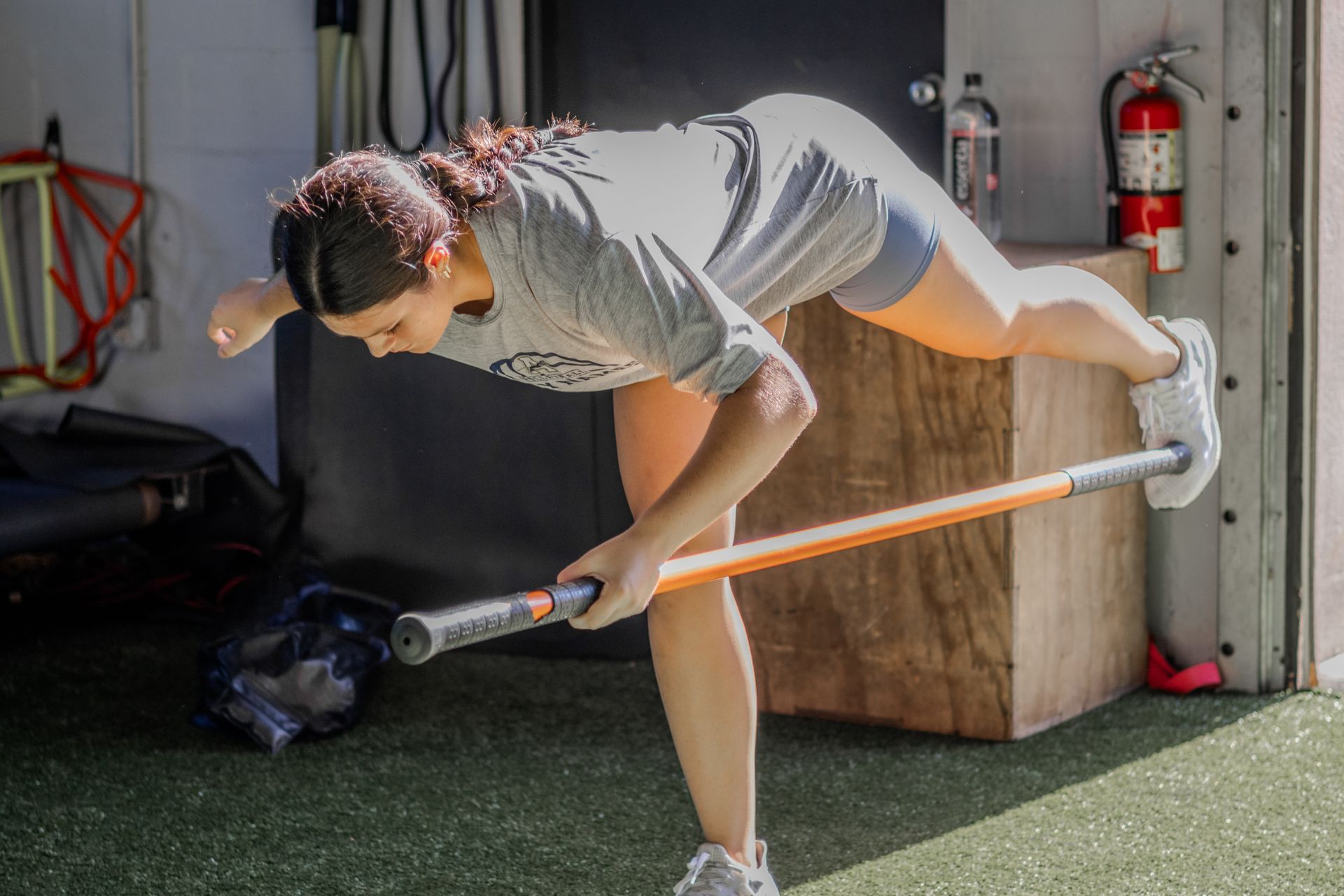 Woman balancing on one leg, reaching with an exercise bar, in a gym.