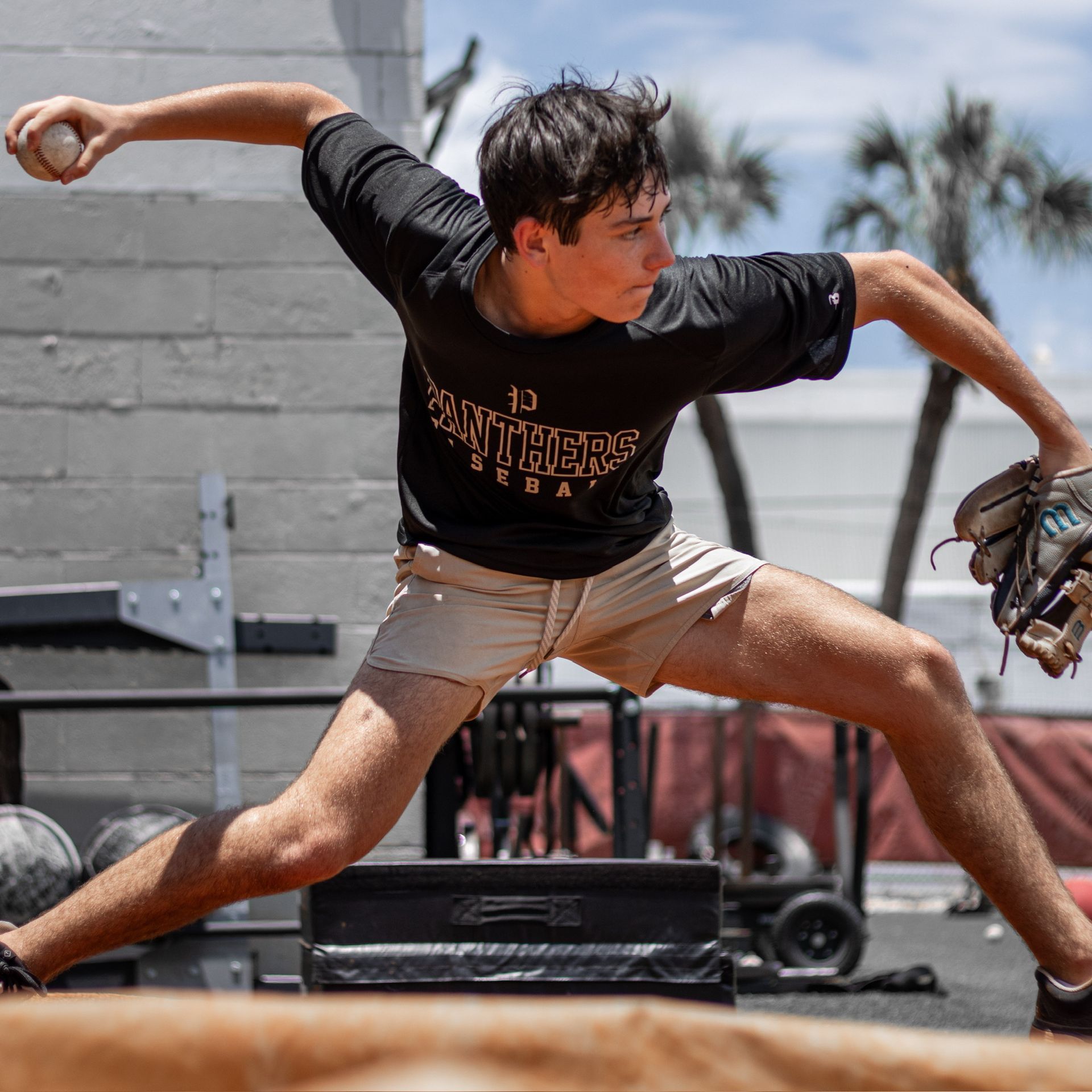 A young man in a baseball uniform pitching a ball outdoors.