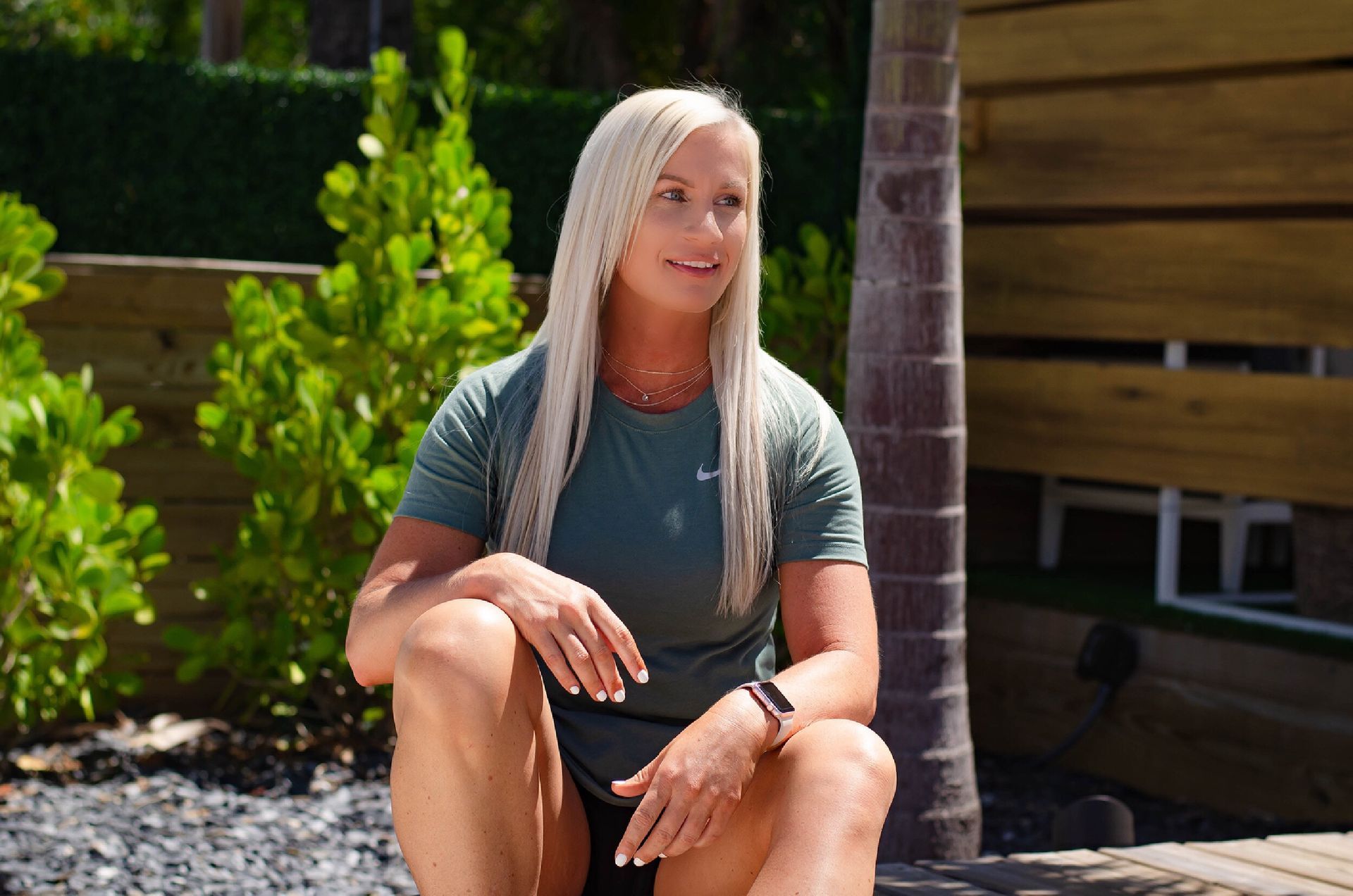 A woman is sitting on the ground in front of a wooden fence.