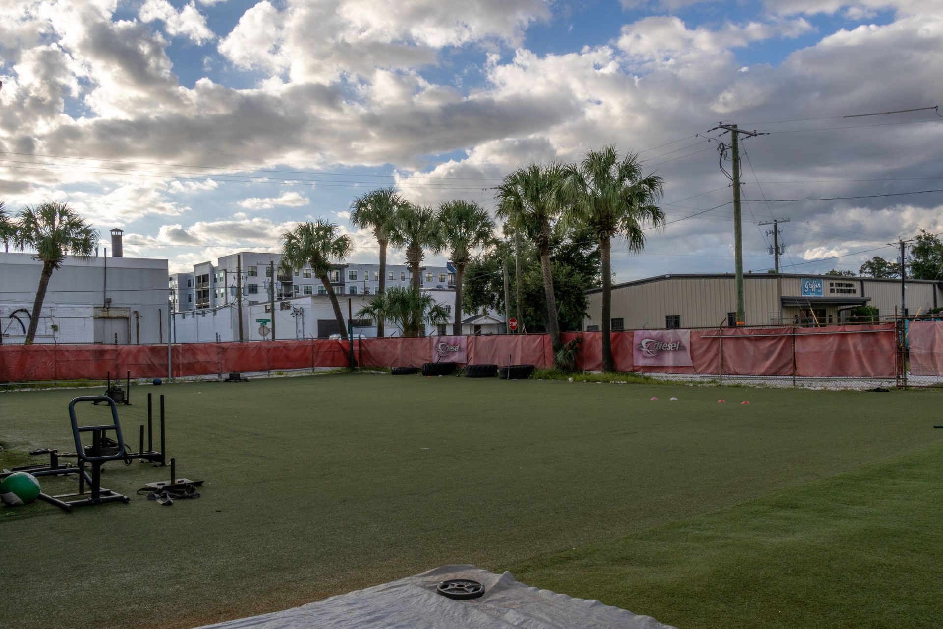 A large empty field with a fence and a few buildings in the background