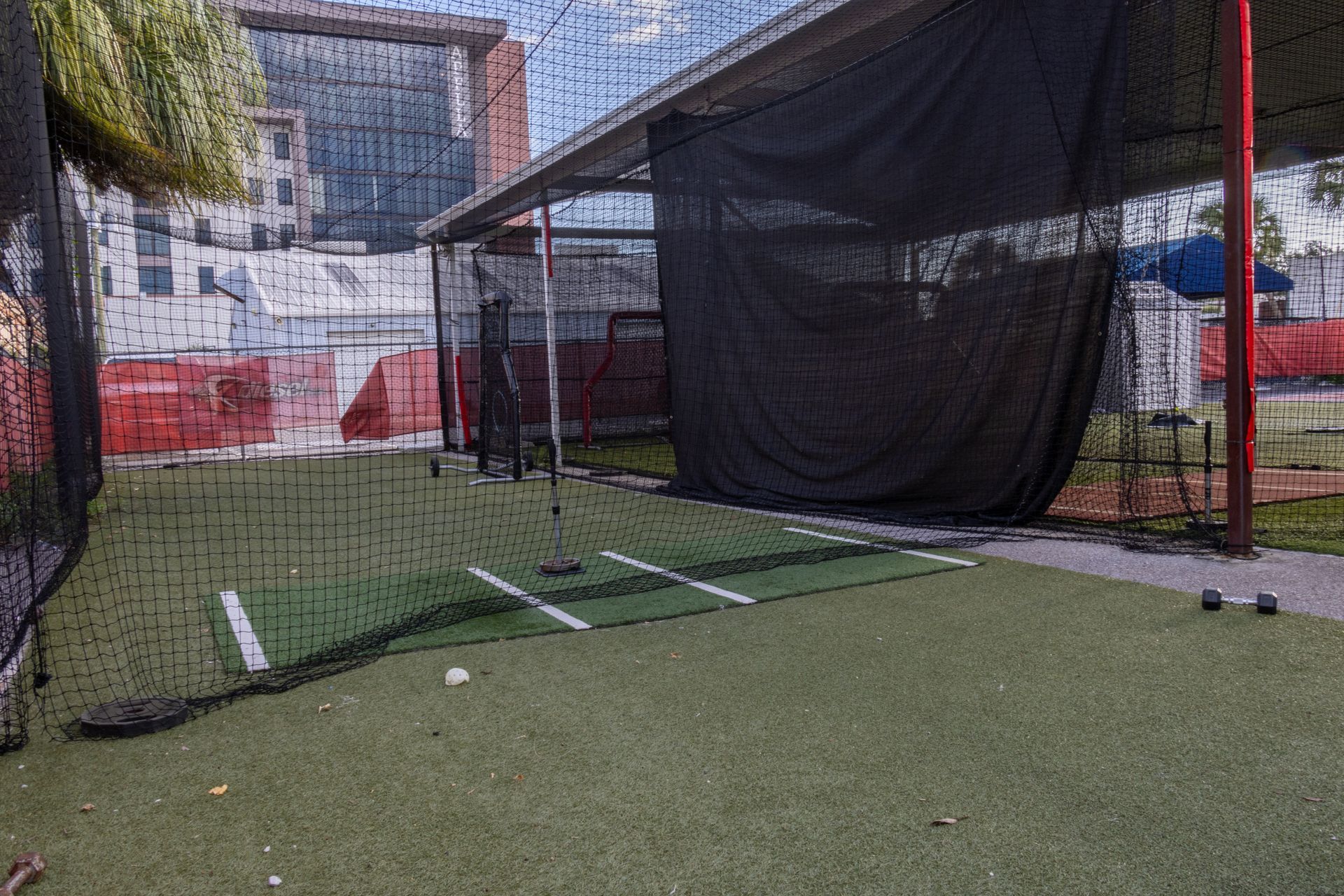 A baseball field with a net and a building in the background.