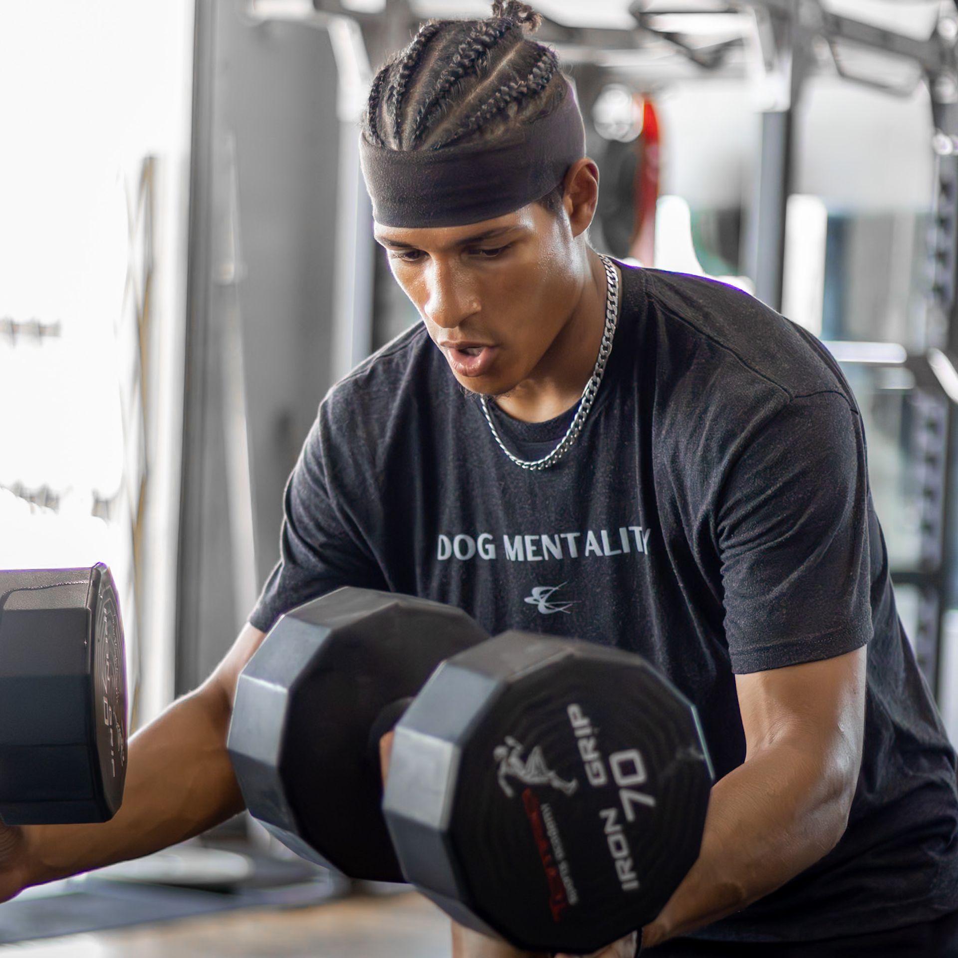 A man wearing a dog mentality shirt is lifting dumbbells in a gym