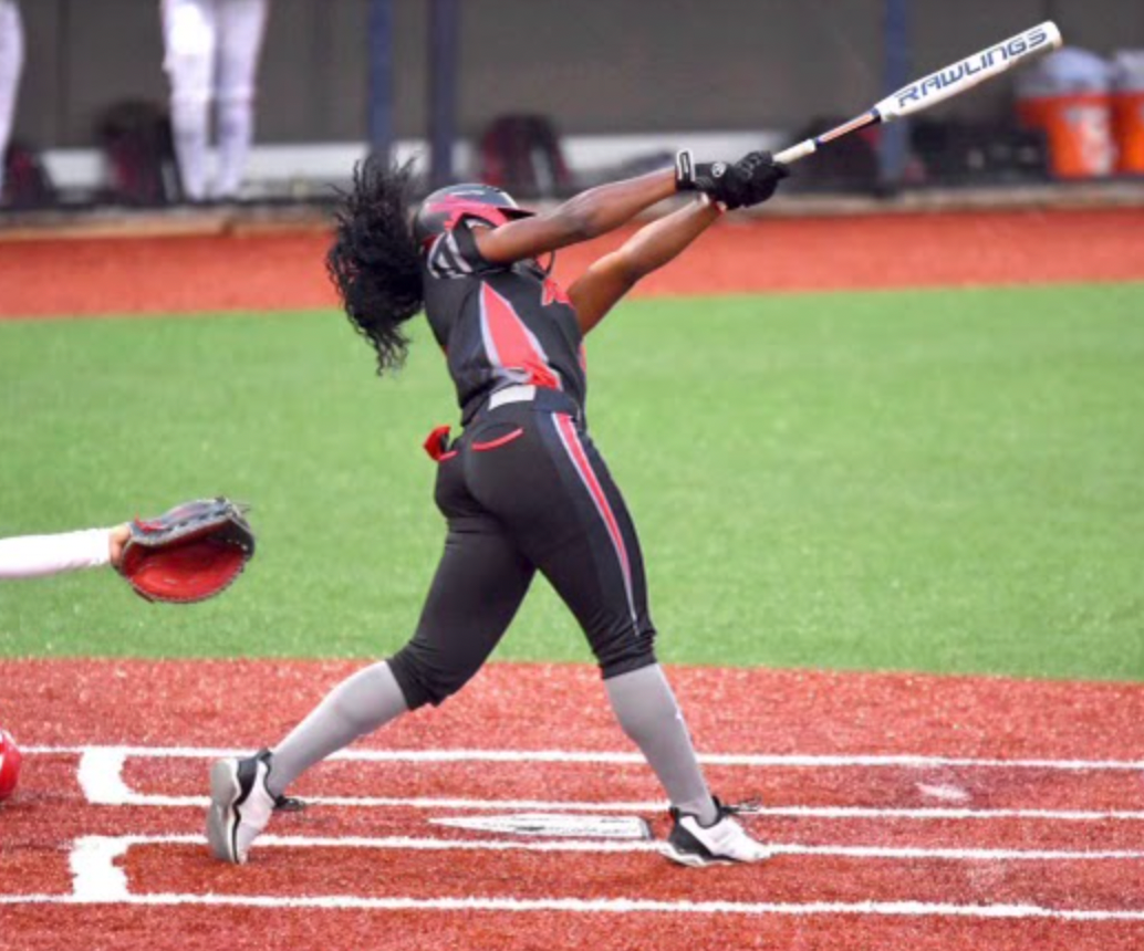 A young girl throwing a softball while being coached on a field with a coach watching.