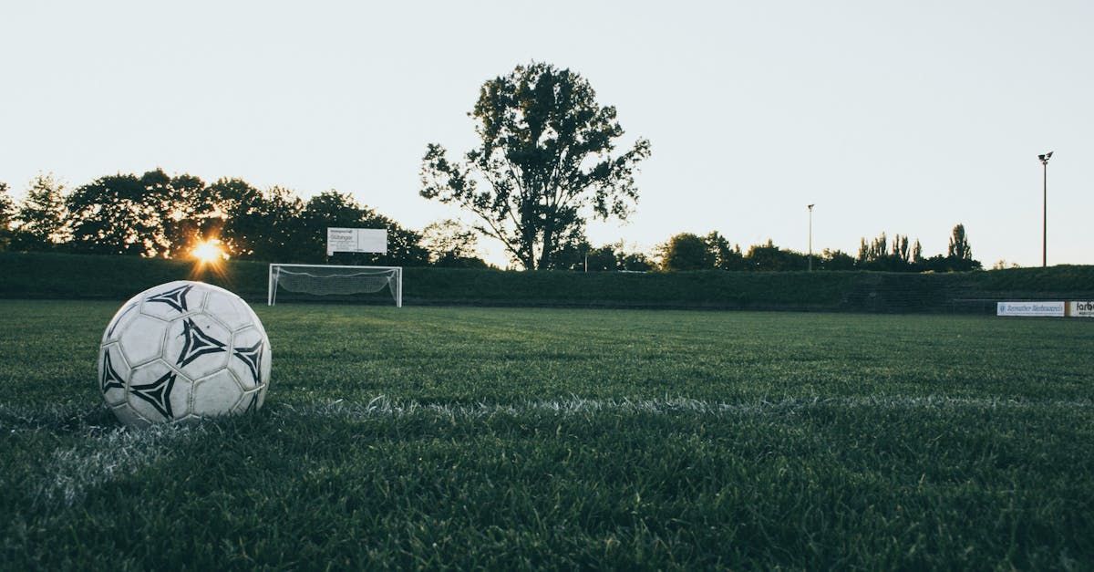 Soccer ball on the field, sunset in the background, goal posts visible.