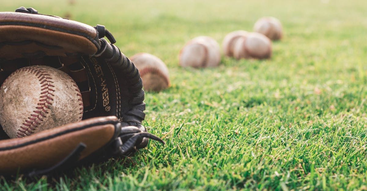 Baseball in glove on green grass with several baseballs in the background.