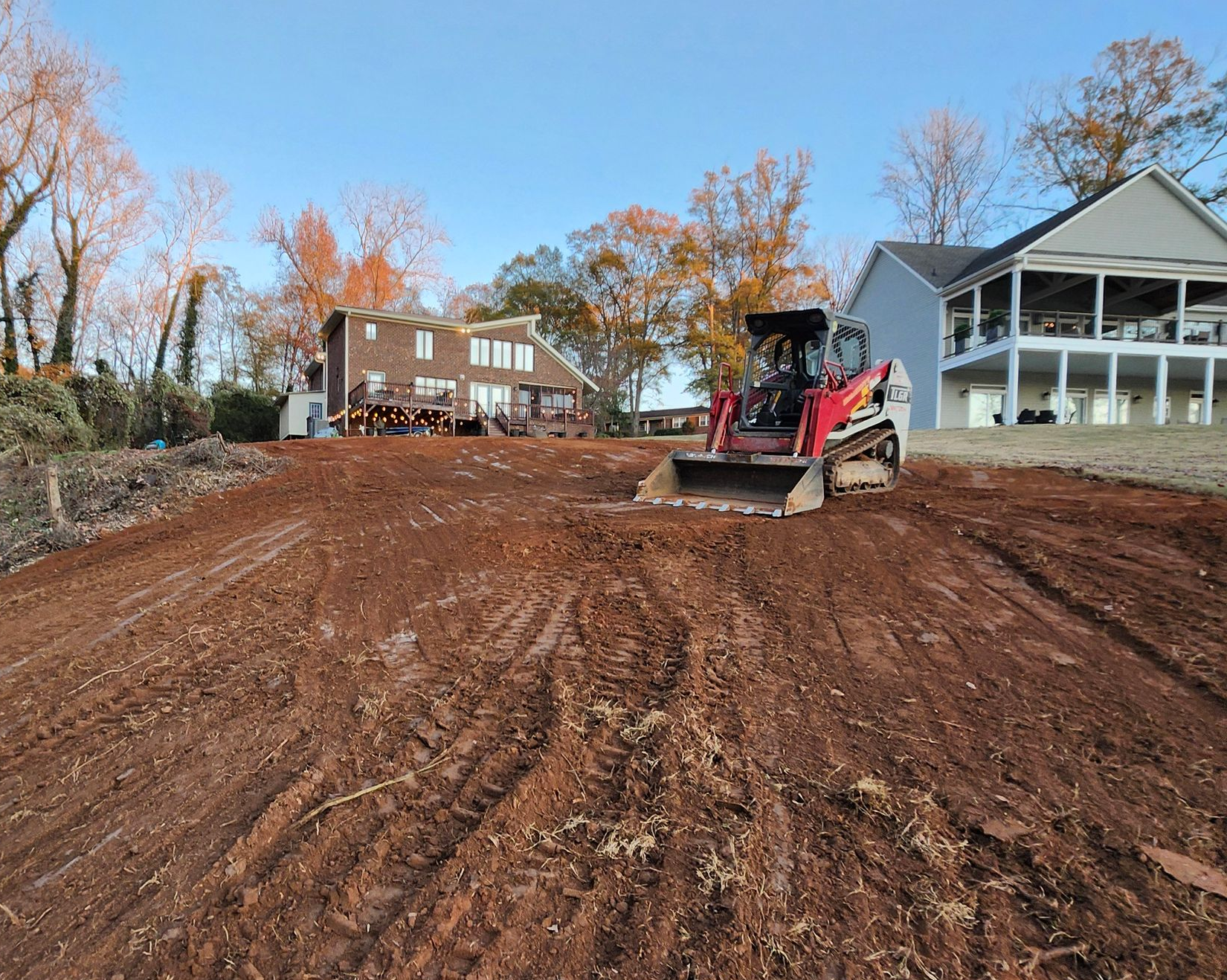 A small excavator is digging a hole in the dirt in front of a house.