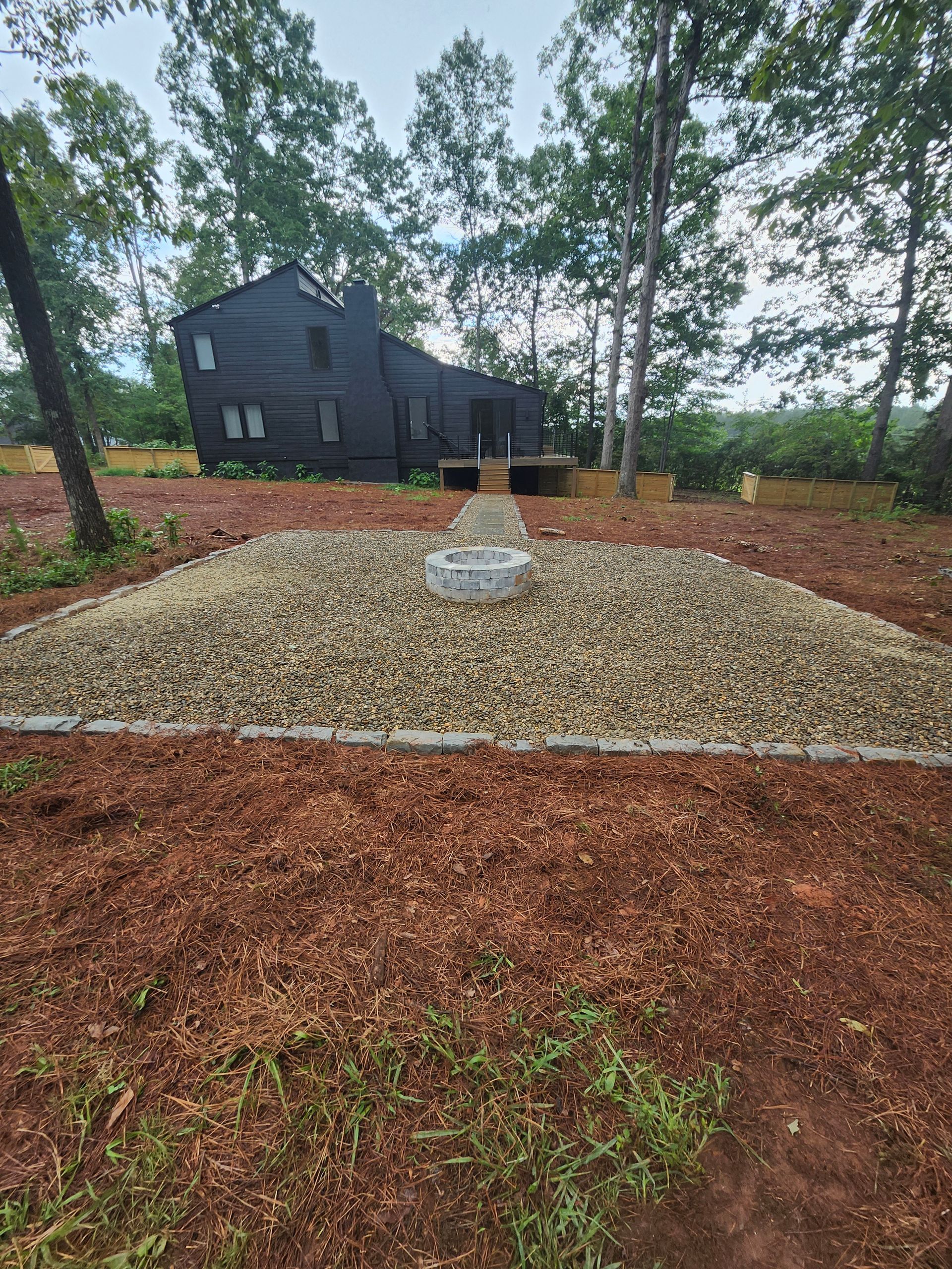 A fire pit is surrounded by gravel in a backyard.
