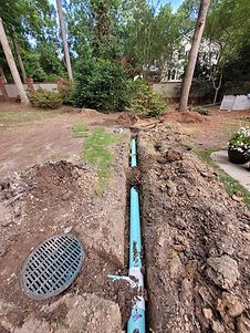 A manhole cover is sitting in the dirt next to a drain pipe.