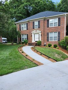 A large brick house with a concrete walkway leading to it.