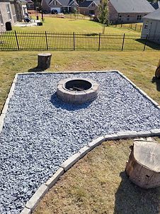 A fire pit is surrounded by gravel in a backyard.