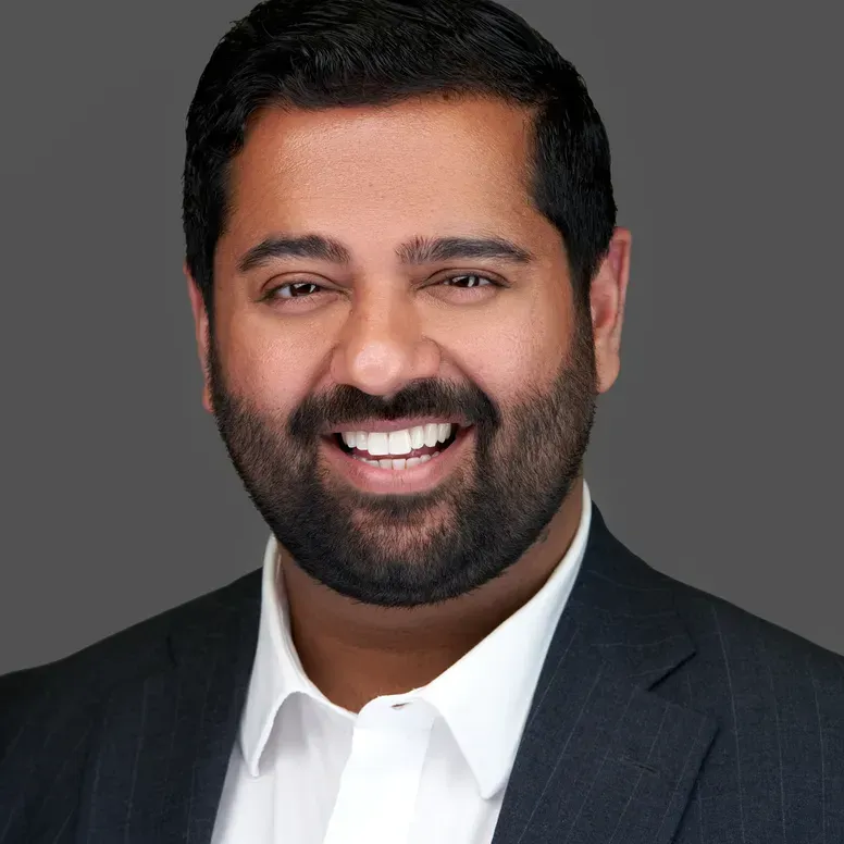 Smiling man in a dark suit and white shirt against a gray background