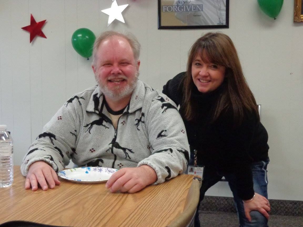 A man sitting at a table with a plate of food and a woman standing behind him