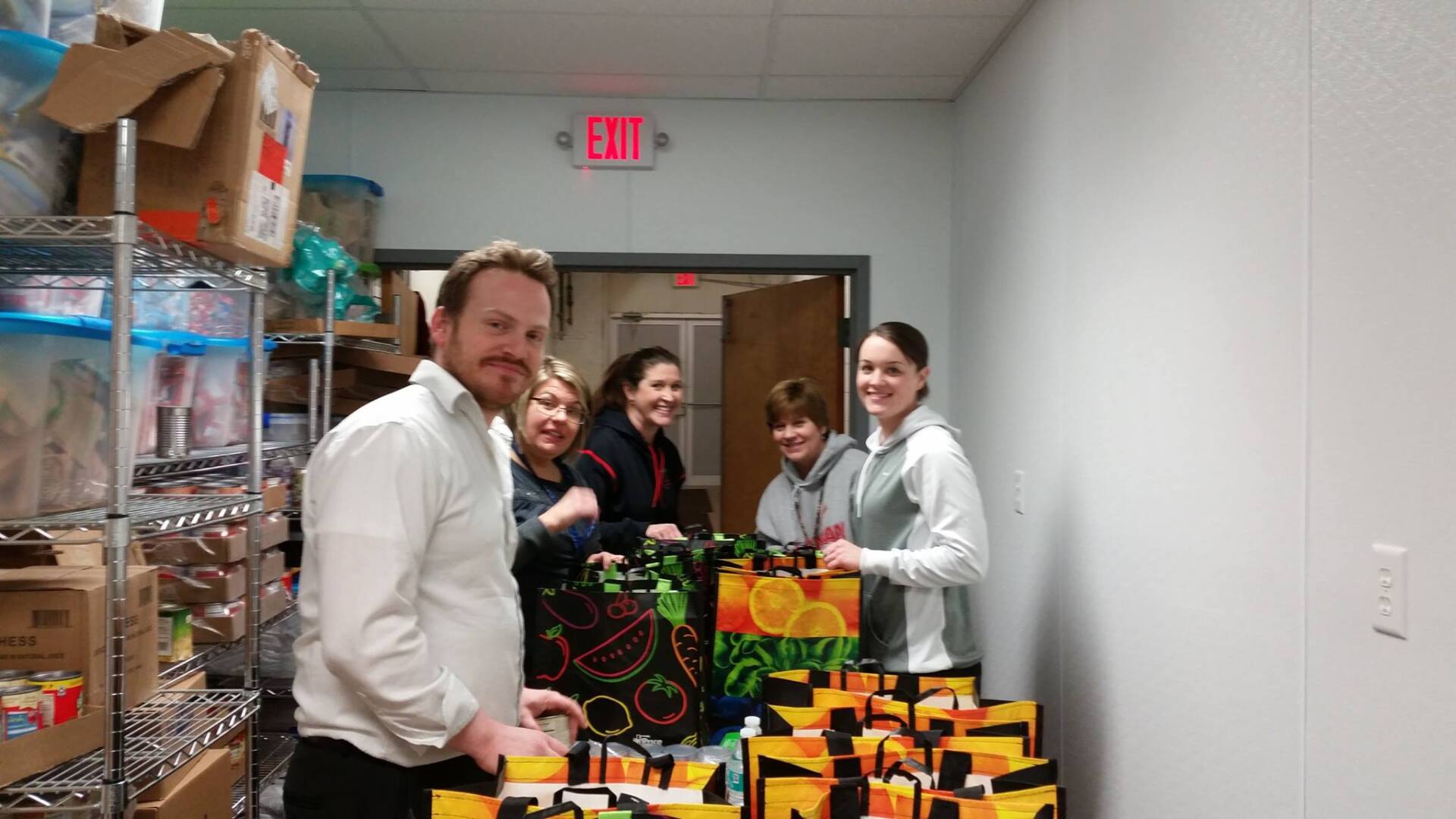 A group of people are standing around a table with bags of food.