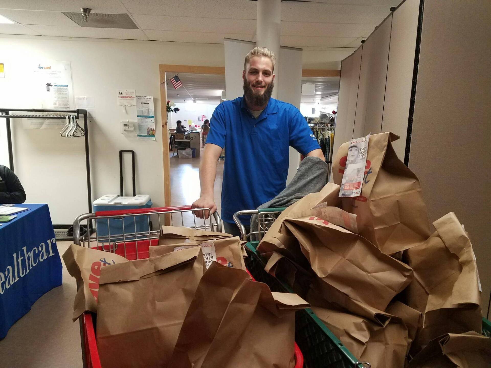 A man in a blue shirt is pushing a shopping cart full of bags