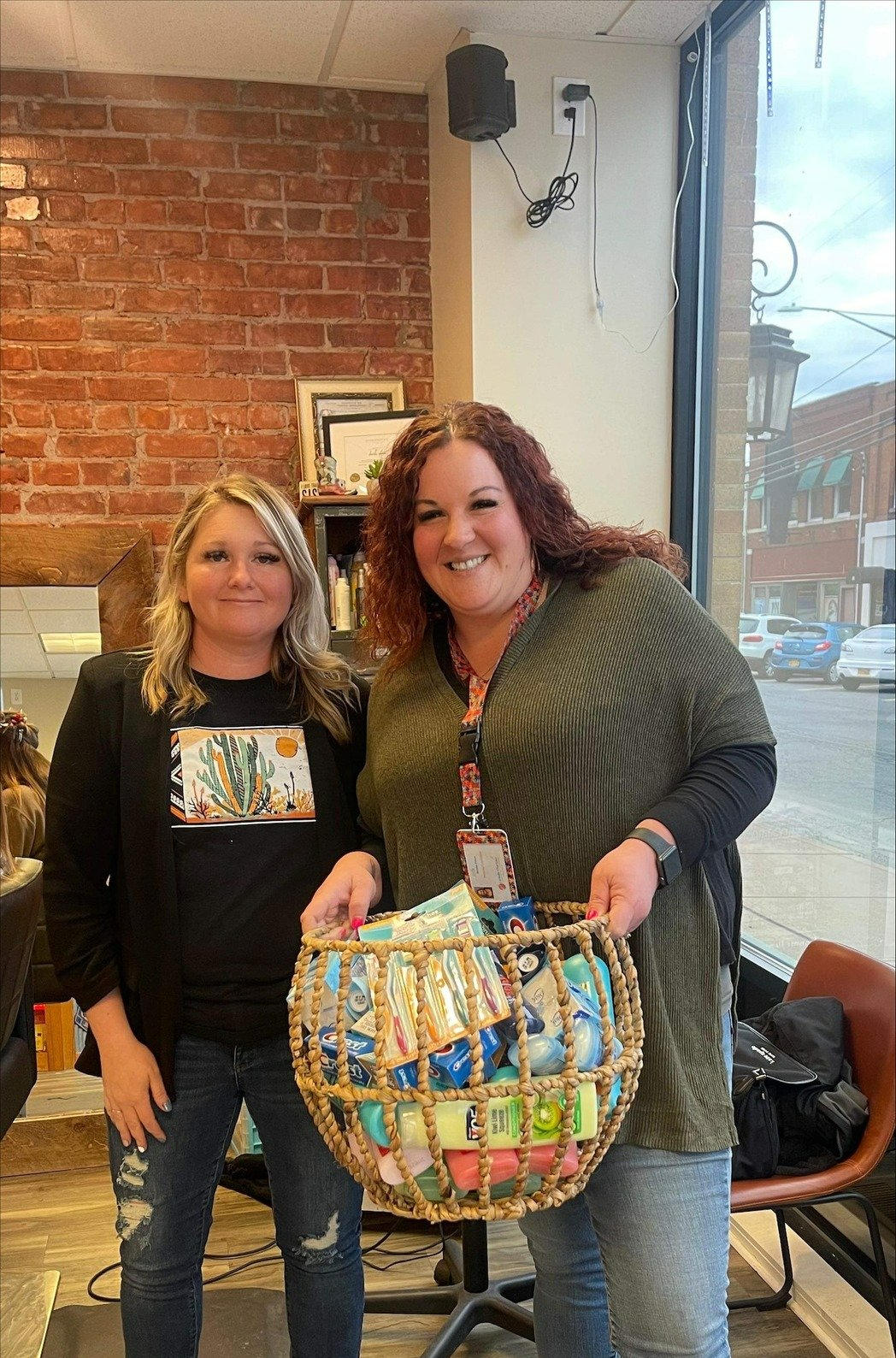Two women are standing next to each other in a salon holding a basket of food.
