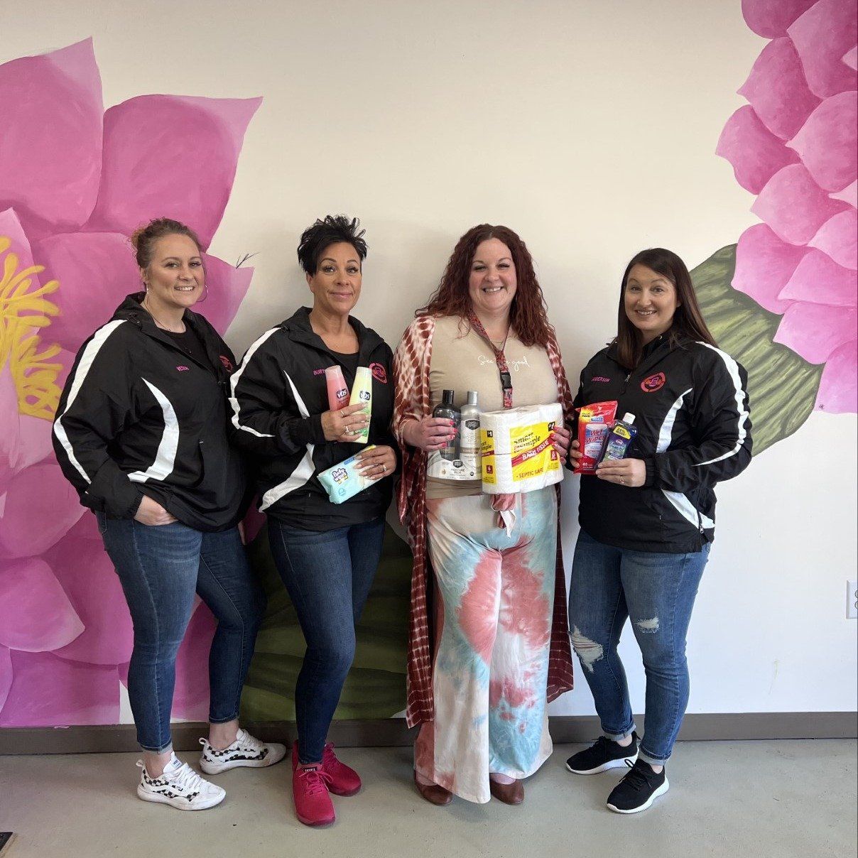 A group of women are posing for a picture in front of a wall with pink flowers.