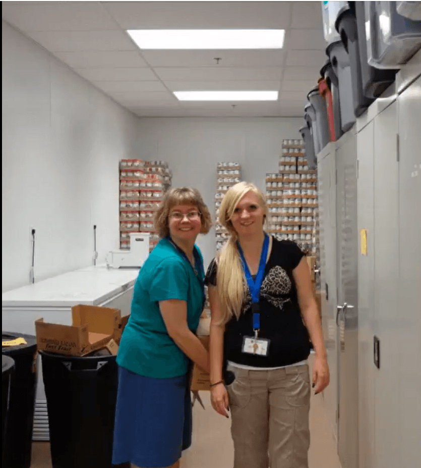 Two women are posing for a picture in a room full of cans