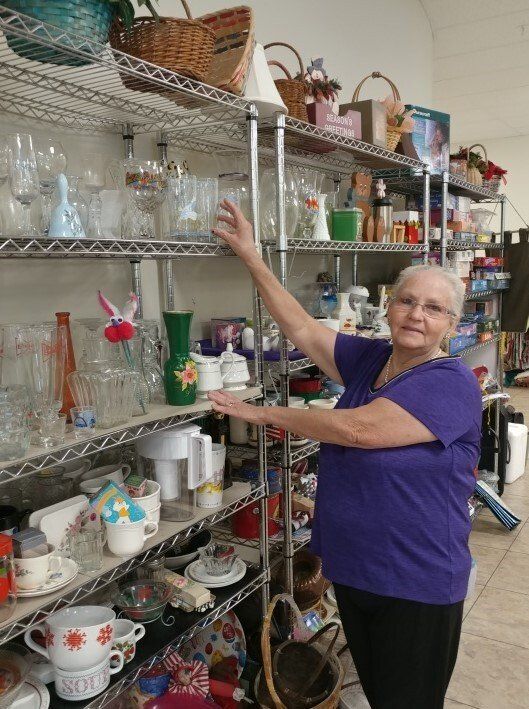 A woman in a purple shirt is reaching for something on a shelf in a store.
