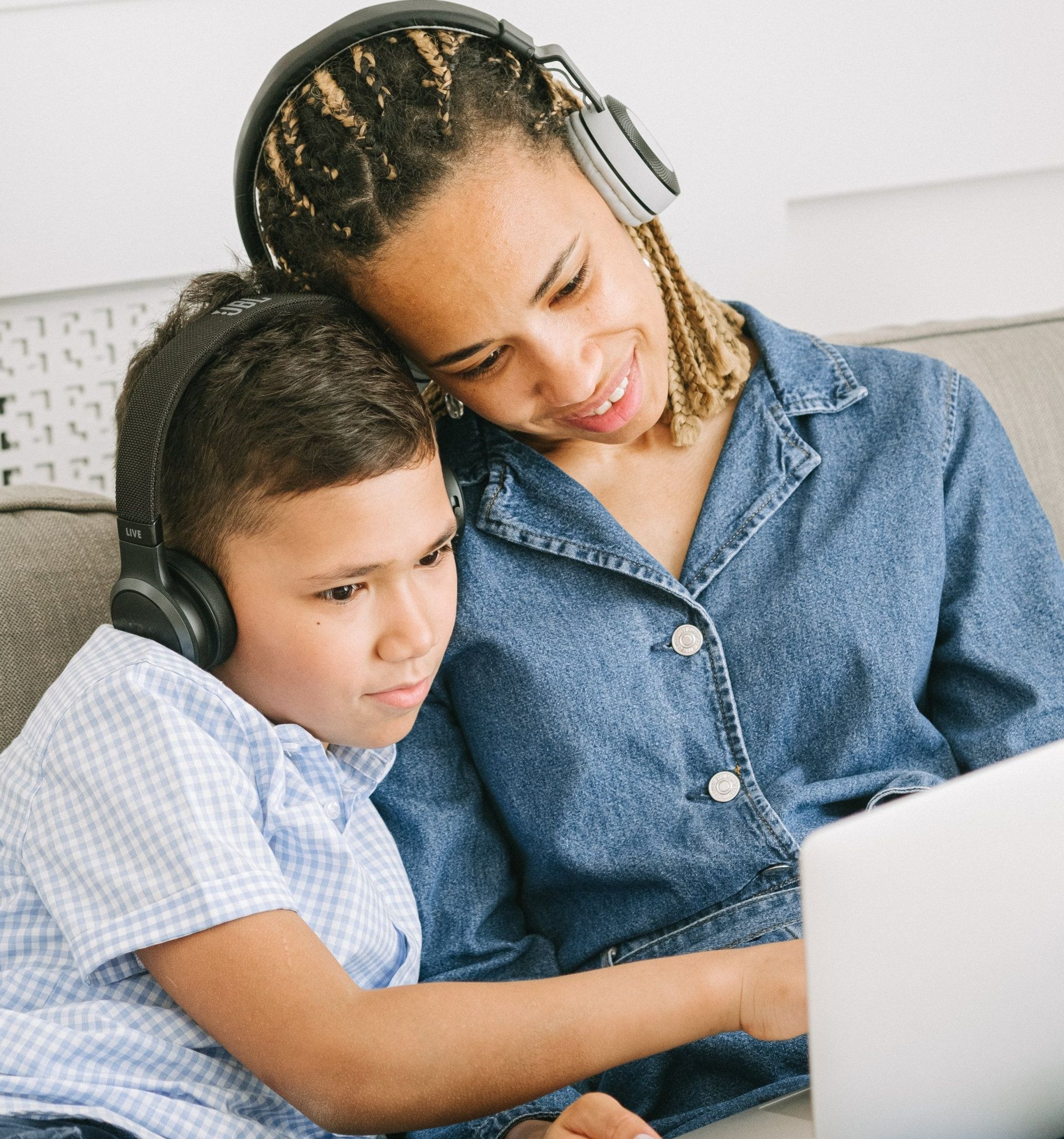 A woman and a child are sitting on a couch looking at a laptop.