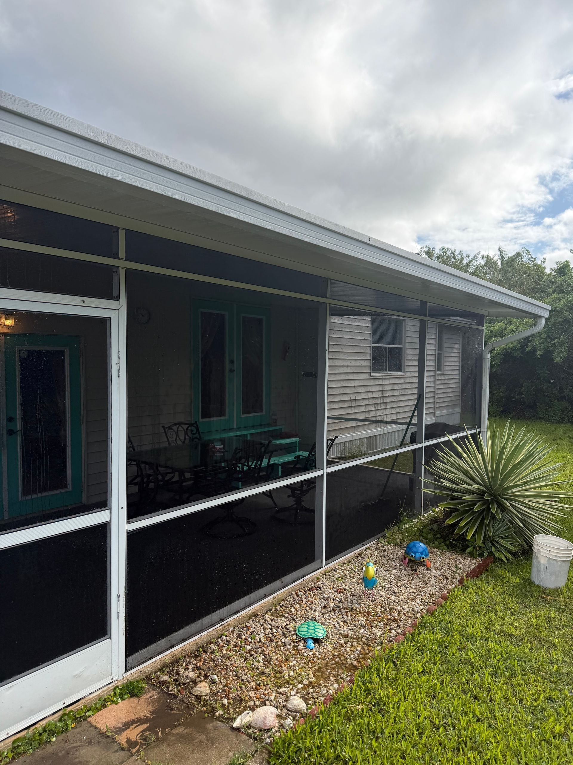 Single-story house with screened porch, white trim, and a small landscaped front yard under cloudy skies