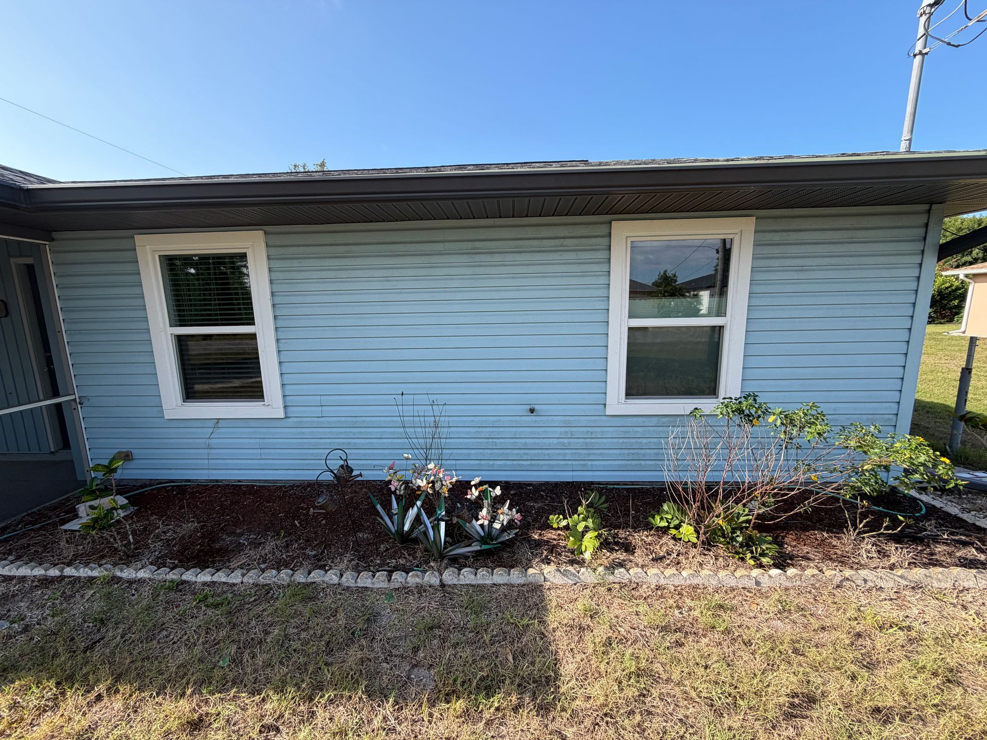 Light blue house exterior with two windows and a small front garden bed