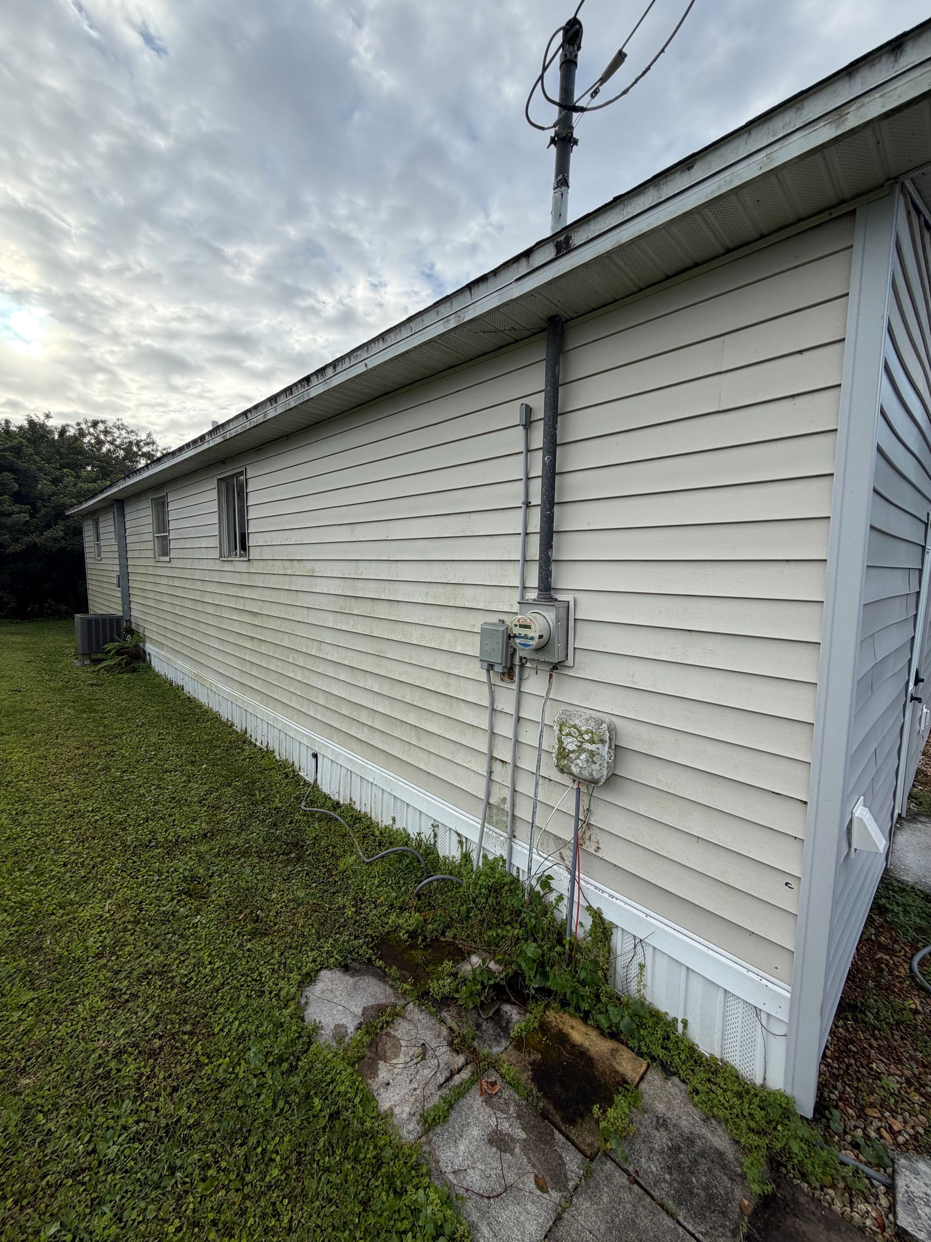 Side view of a white house with vinyl siding, utility meter, and grassy yard under a cloudy sky
