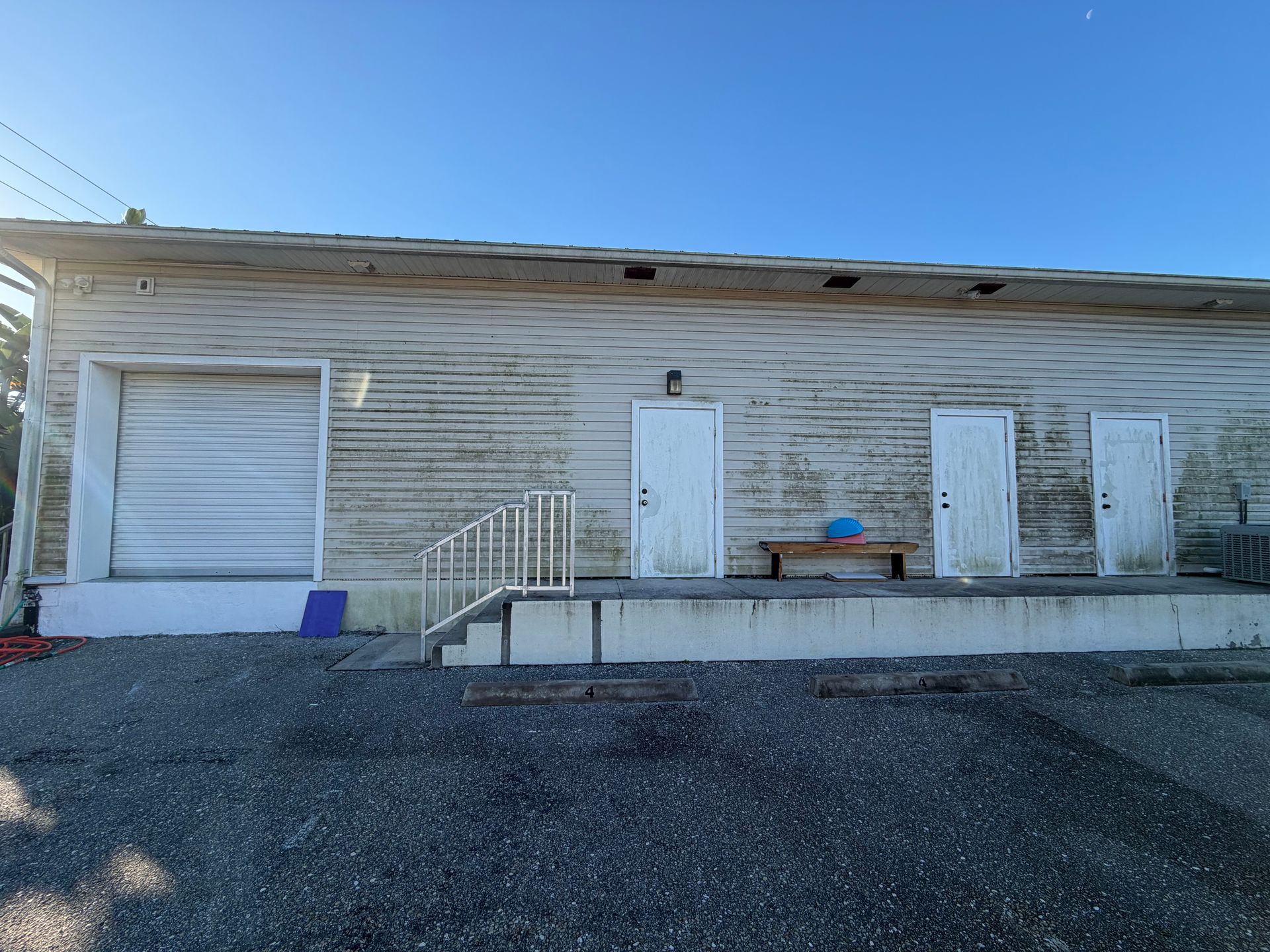 Weathered single-story building with a ramp, two doors, and gravel foreground under a clear blue sky