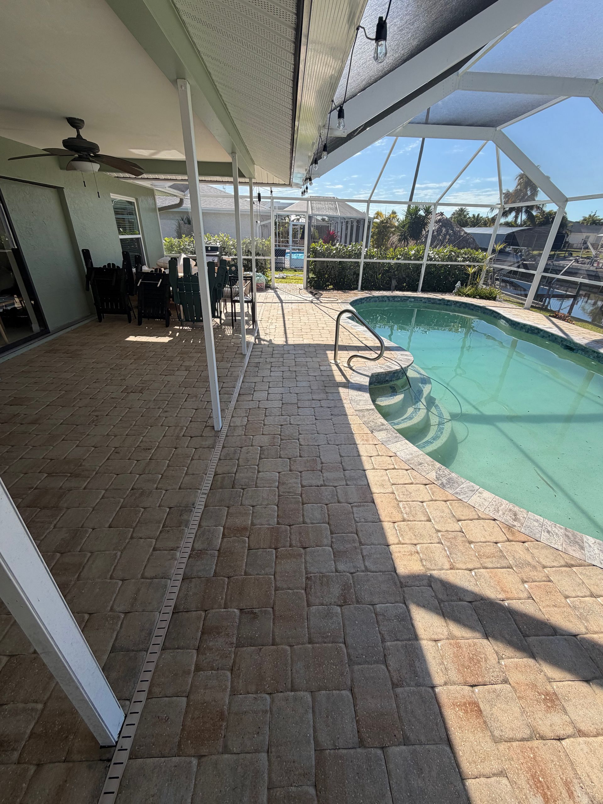 Covered patio beside a swimming pool with brick pavers and backyard landscaping