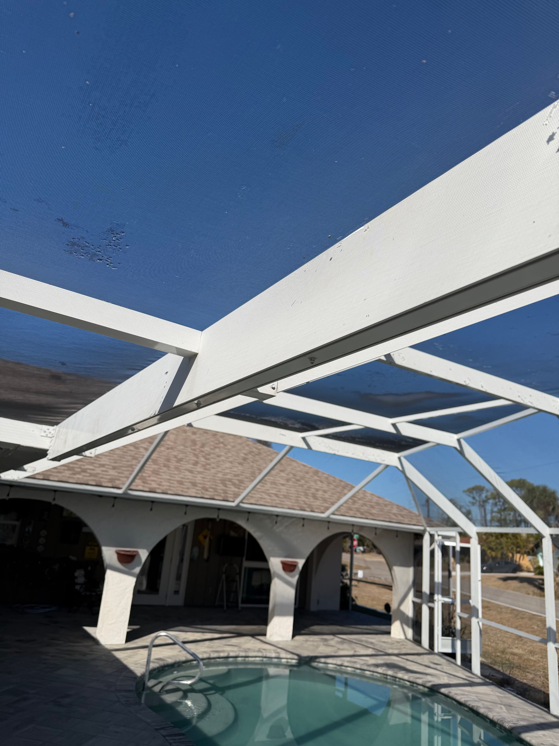 White patio shade structure over a pool beside a brick house under a blue sky