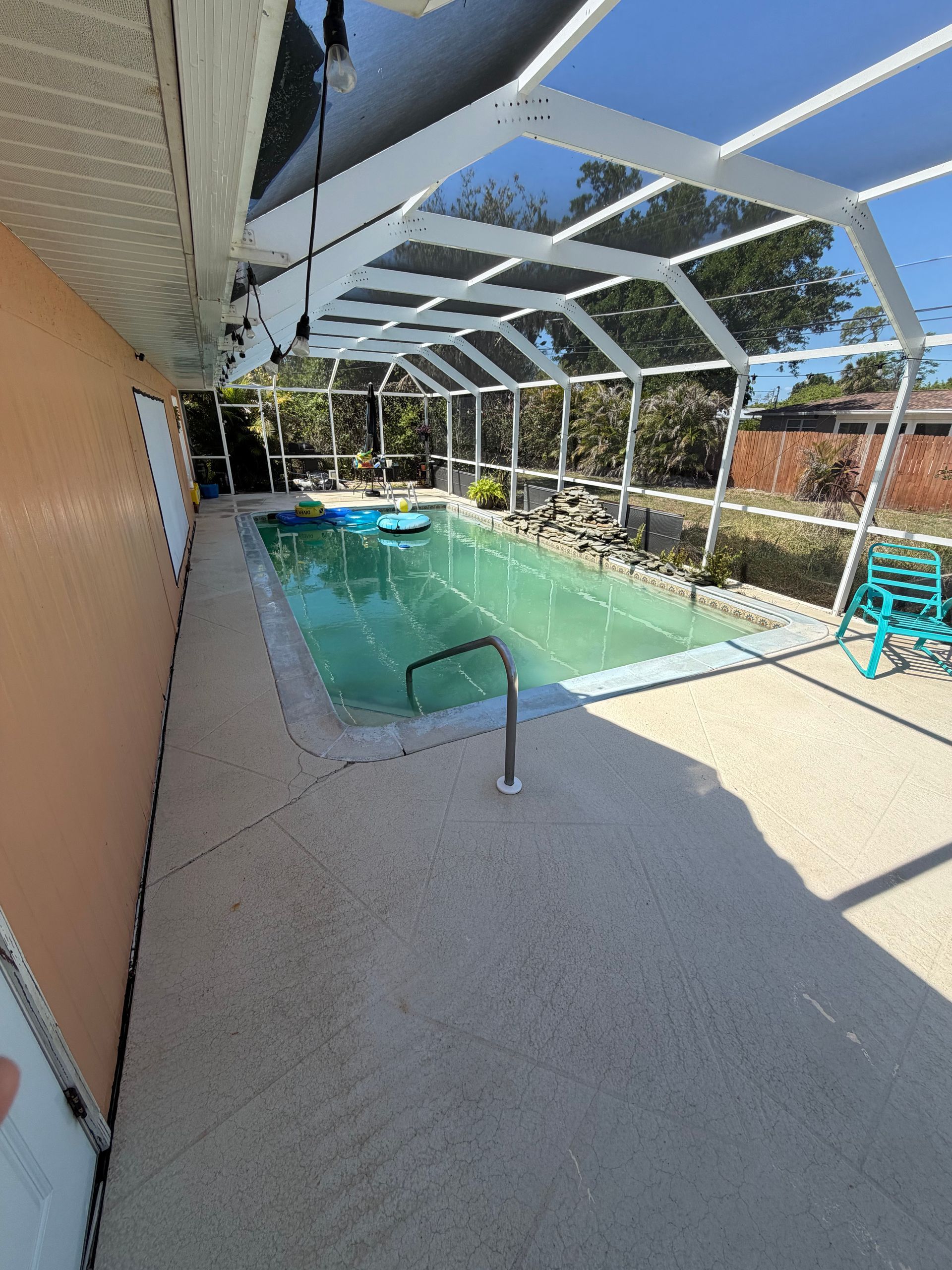 Covered backyard pool with blue water, white screened enclosure, and patio railing in sunlight