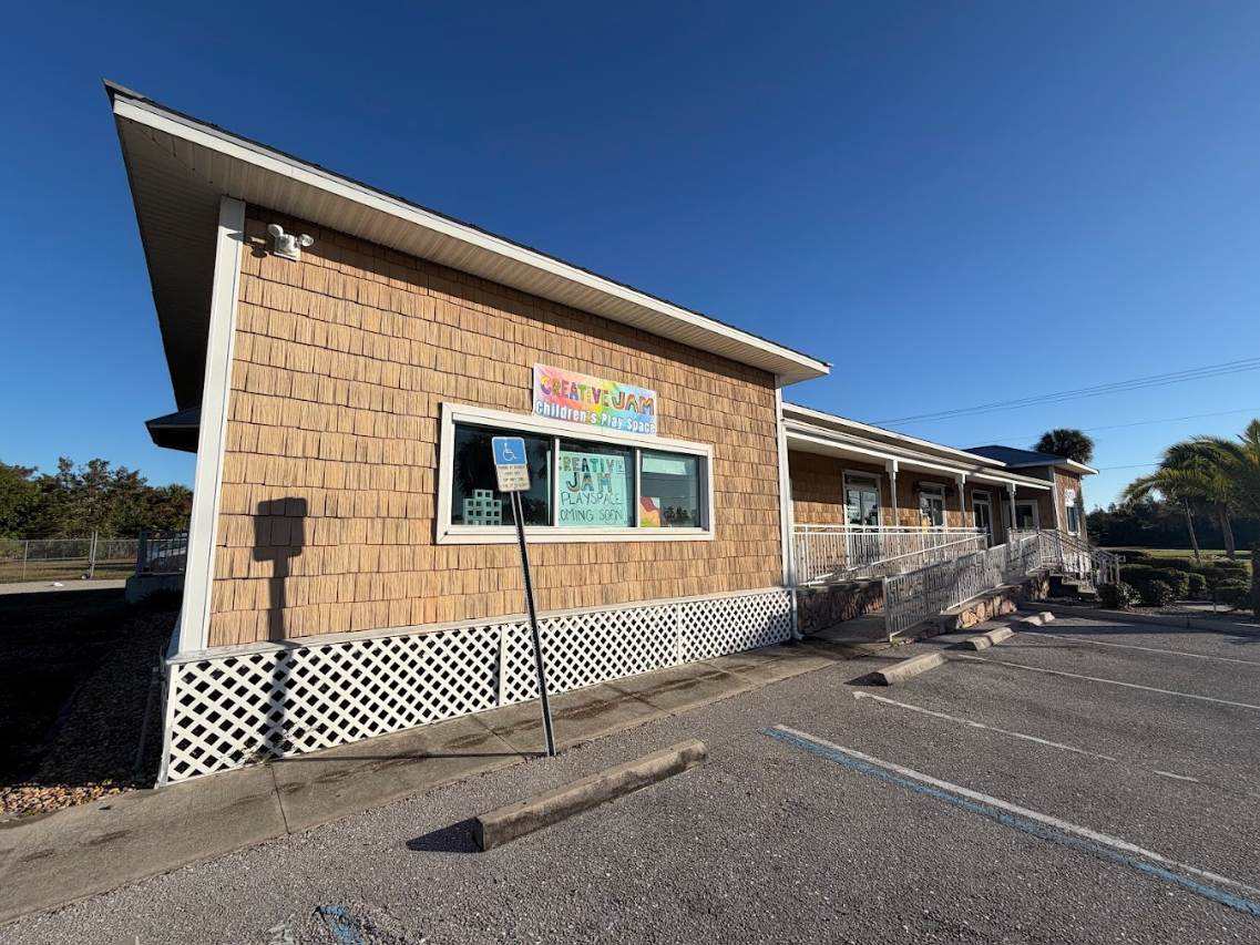 Driveway leading to a large light blue house with lush landscaping and trees.