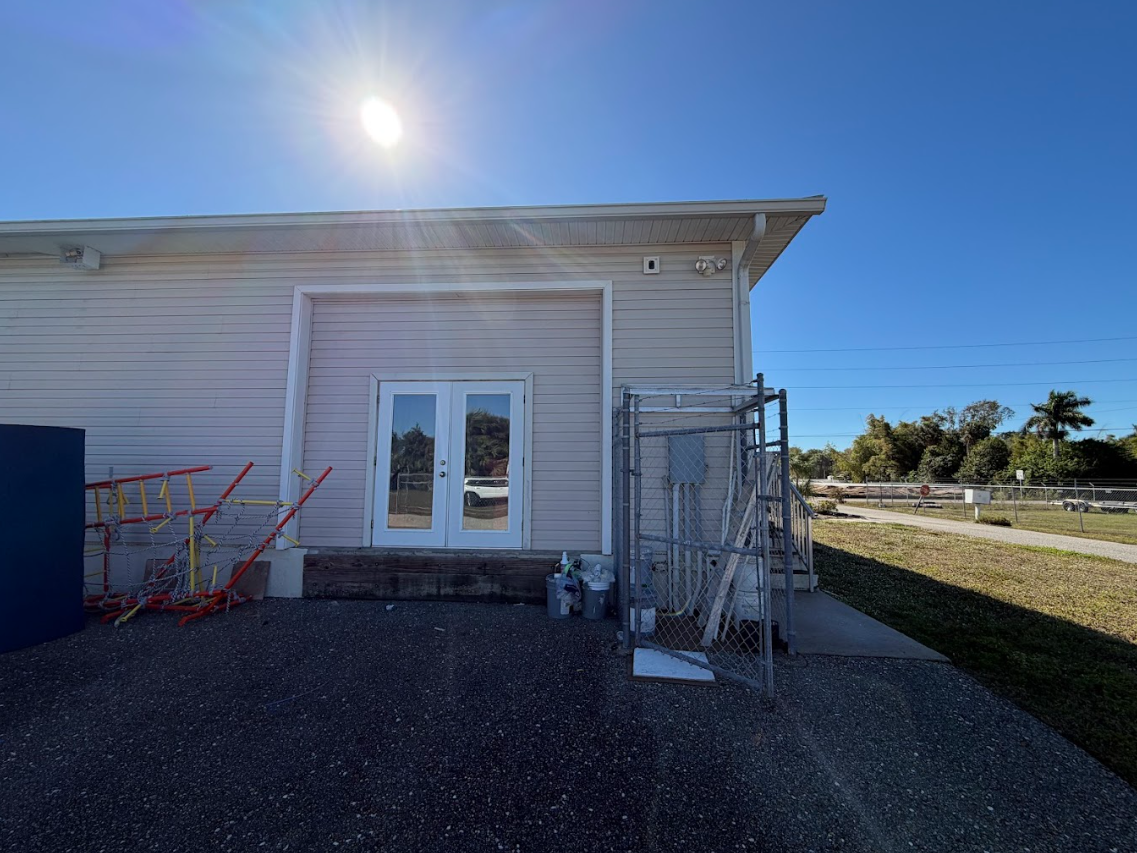 Driveway paved with textured stones, flanked by green grass and a silver SUV parked in front of a house. Palm tree shadow.