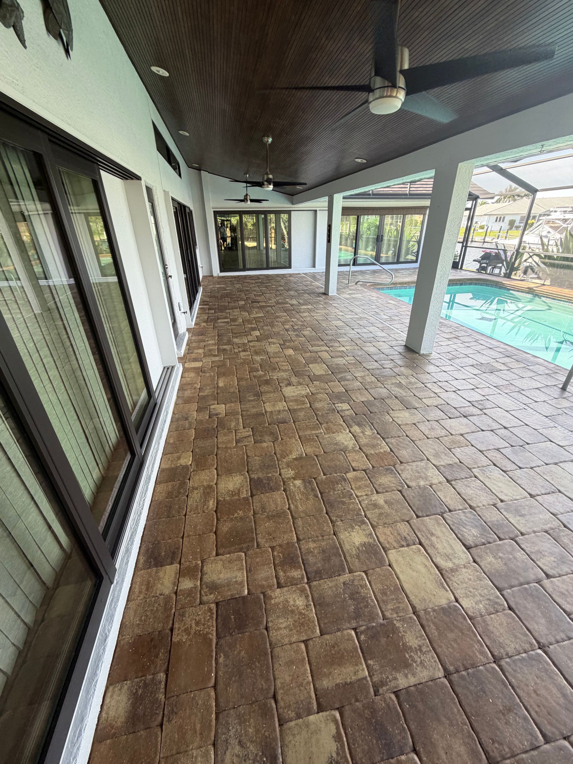 Covered patio with brown tile floor, ceiling fan, sliding glass doors, and pool view