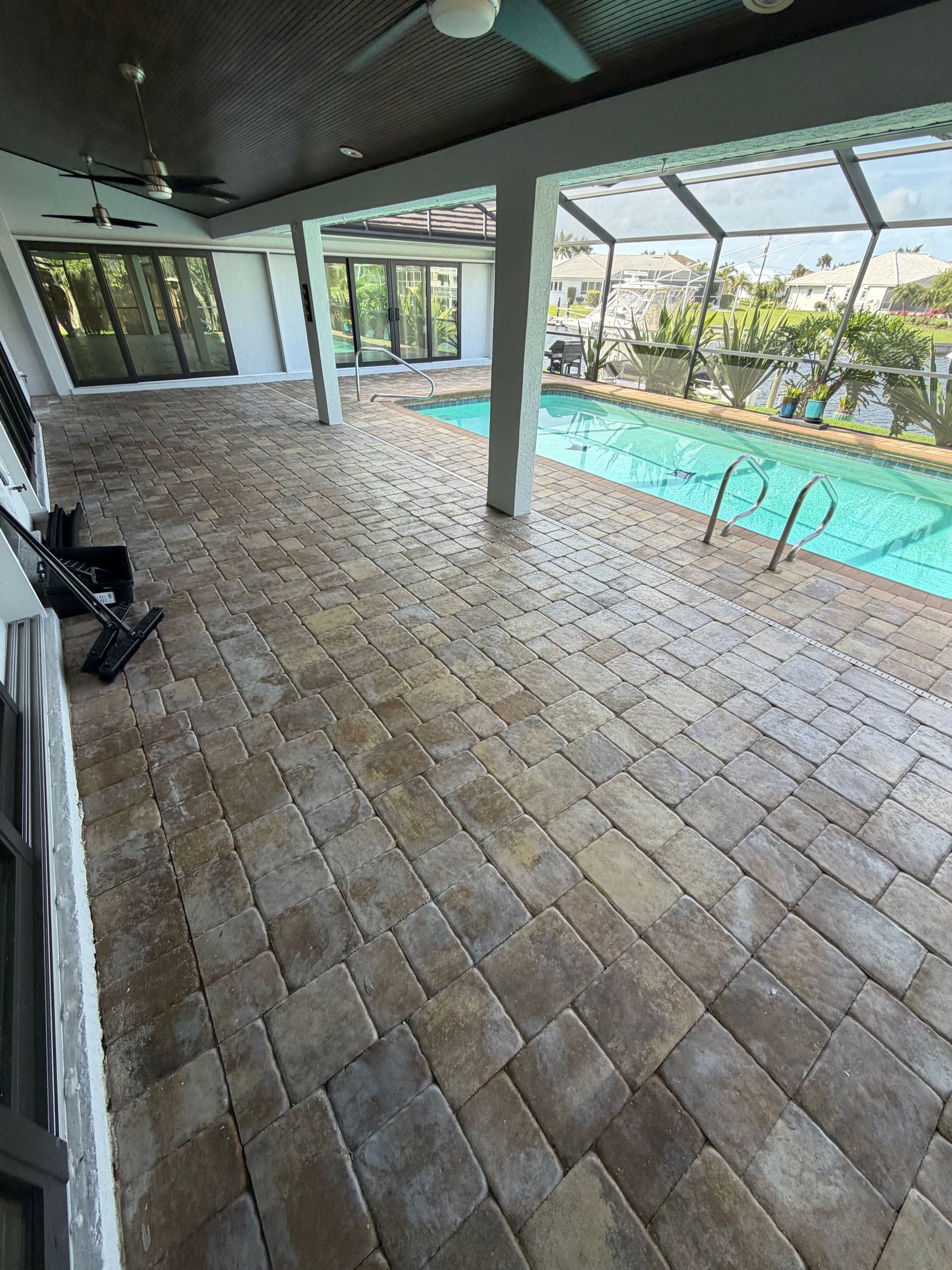 Covered patio beside a blue swimming pool, with stone tile flooring and screened enclosure.