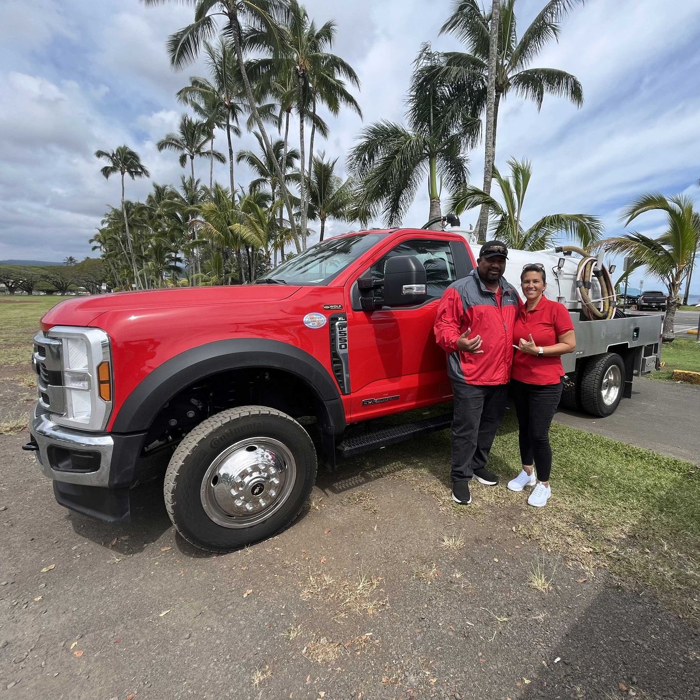 Two people stand next to a red flatbed truck. Man is wearing a red jacket and black pants. 