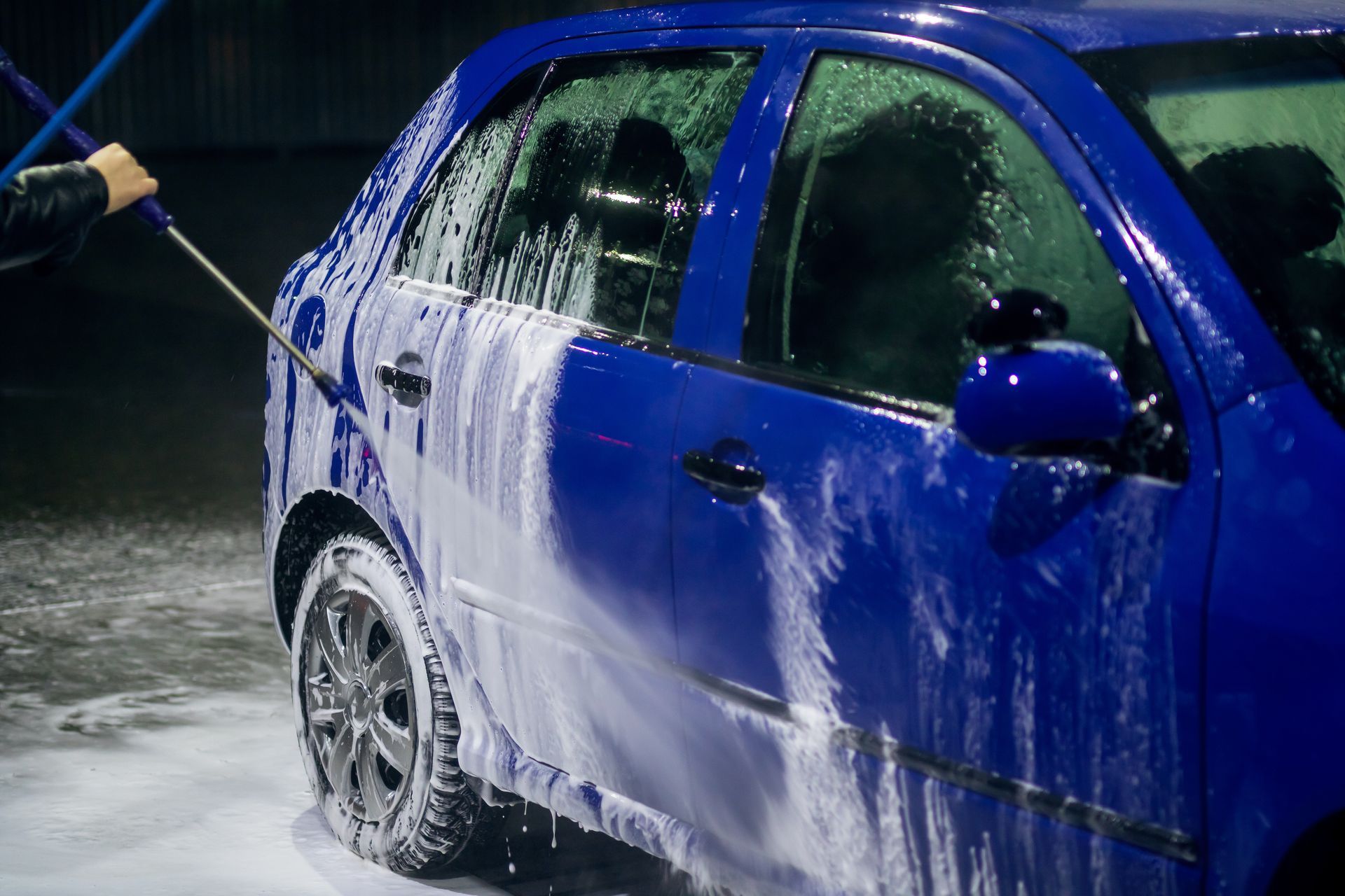 A person is washing a blue car with a high pressure washer.