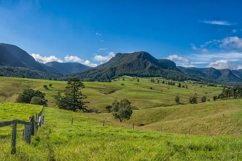 Rolling Green Hills with A Wooden Fence and Distant Mountains Under a Blue Sky — Tomac Civil In Southeast Queensland, QLD
