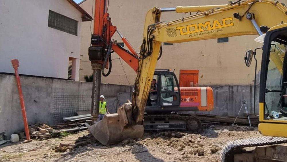 Drilling Machine Excavating Rock Face in A Quarry. Orange and White Machinery in A Dusty, Rocky Setting — Tomac Civil in Brisbane, QLD 