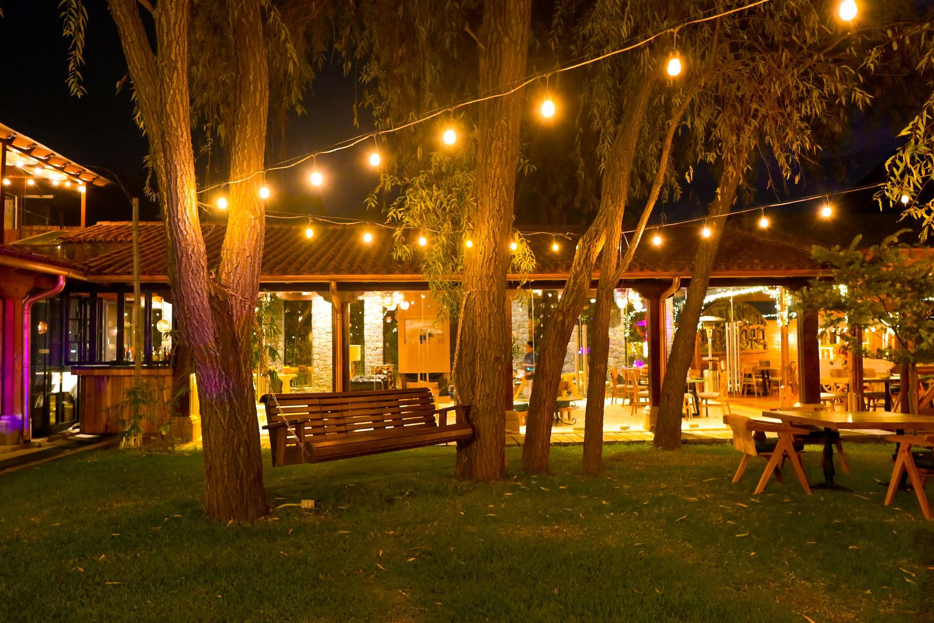 Un columpio de madera está sentado debajo de un árbol en un parque por la noche.