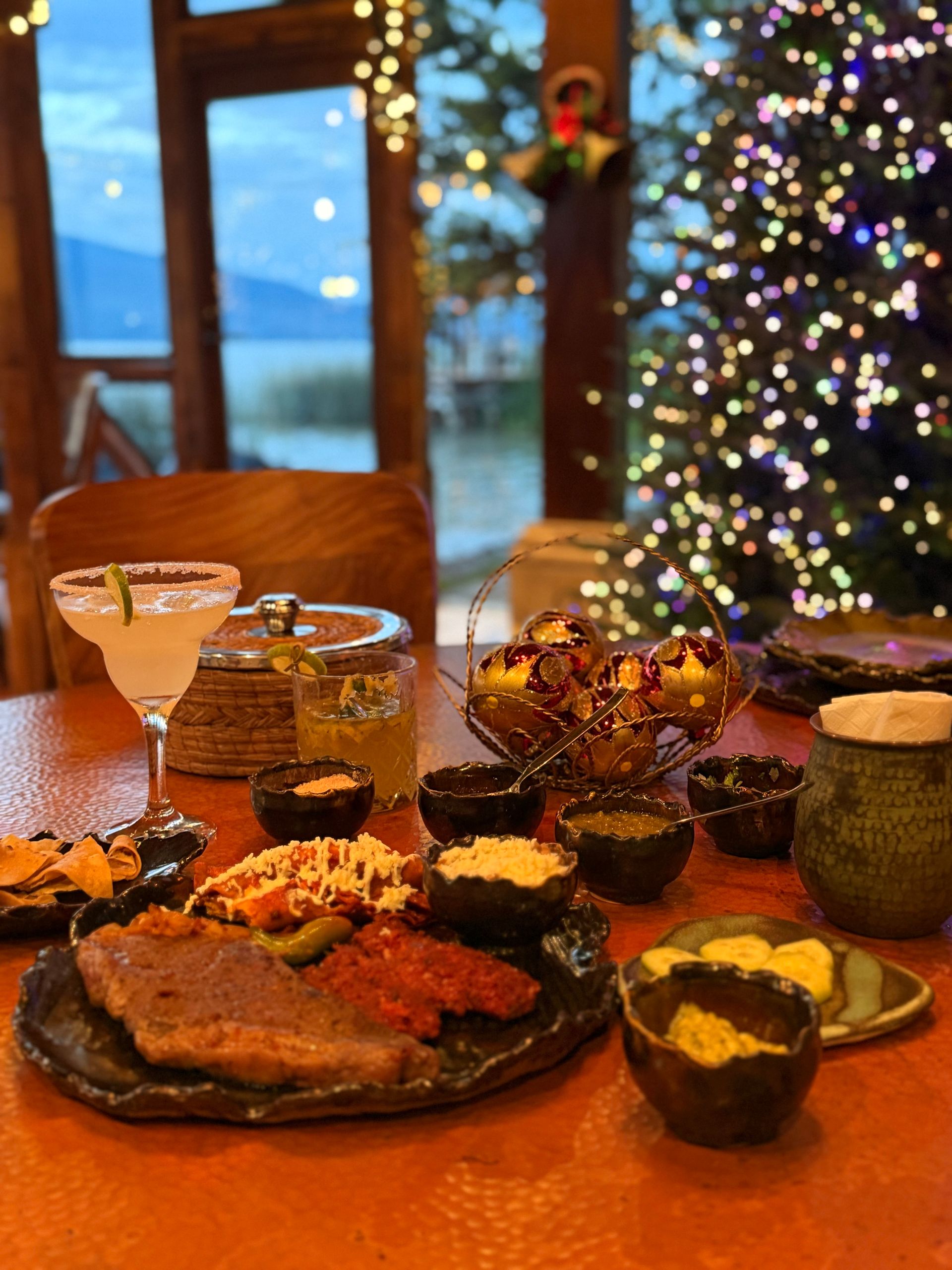 Una mesa cubierta con platos de comida y bebidas con un árbol de Navidad al fondo.