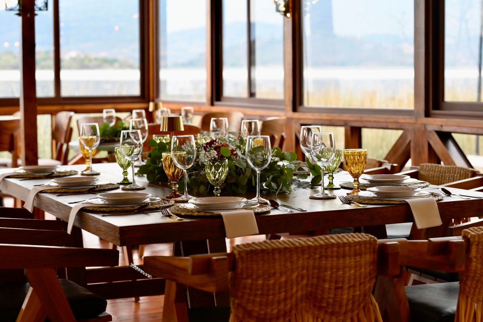 A dining room table with plates , glasses , and a vase of flowers on it.