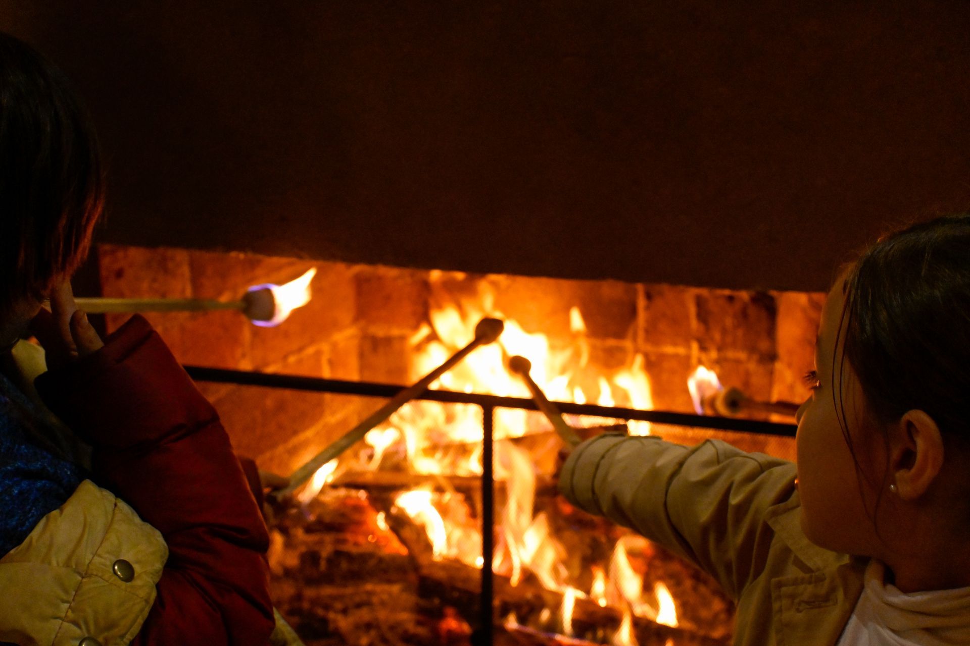 Dos niños están asando malvaviscos frente a una chimenea.