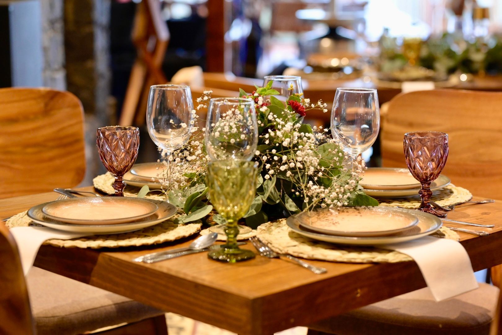 Una mesa de madera con platos, vasos y flores sobre ella.