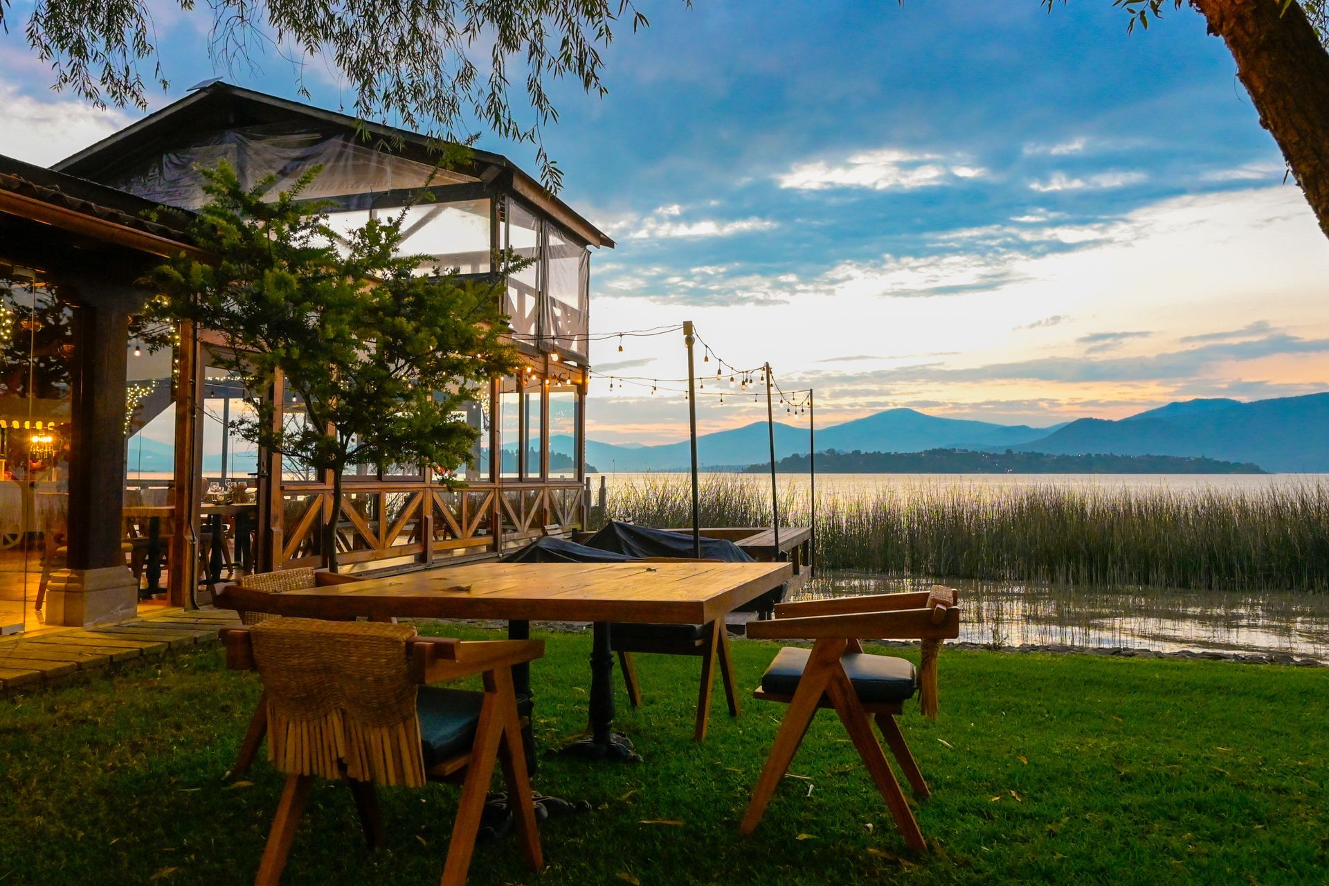 Una mesa y sillas de madera están colocadas en el césped cerca de un lago.