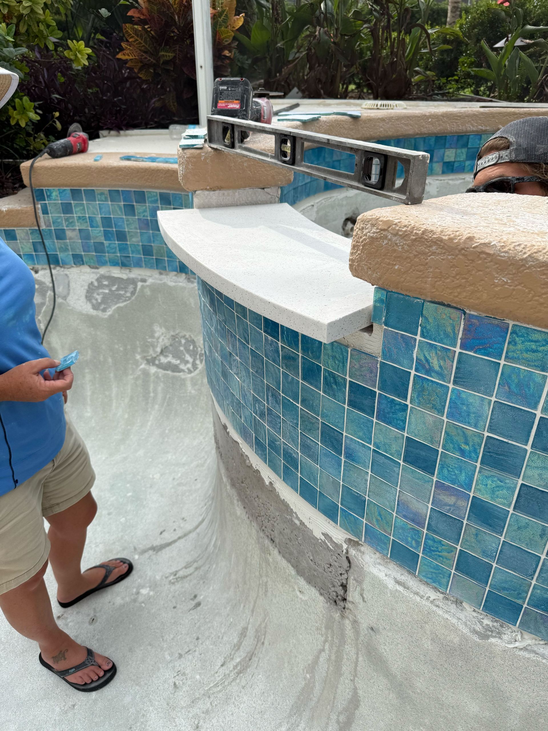 Pool construction: Worker checks level of a stone ledge with blue tile surround.