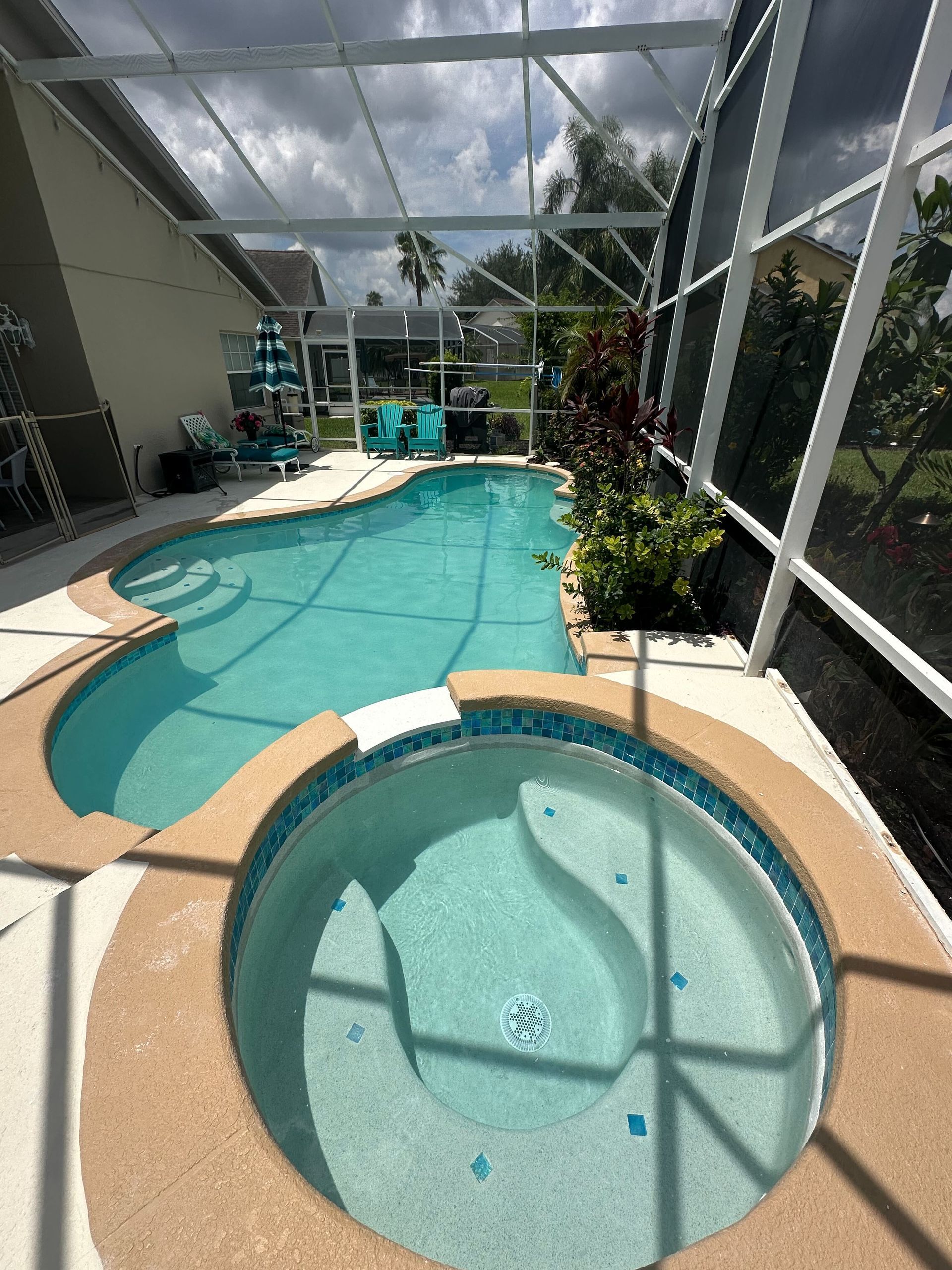 Swimming pool and hot tub enclosed by a screen. The pool has a curved design, with two lounge chairs in the background.