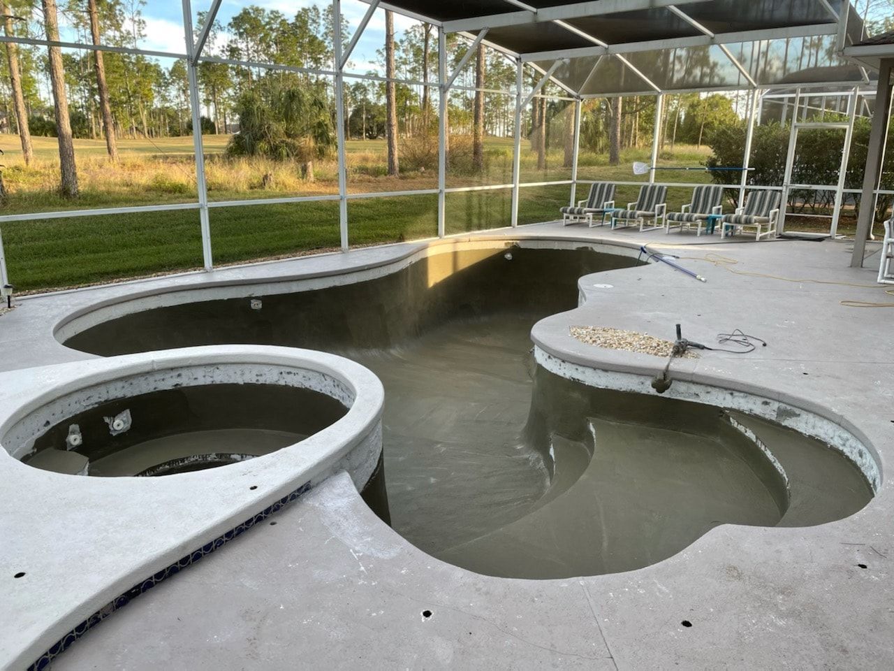 A newly constructed swimming pool with an attached spa, enclosed by a screen structure, in a backyard setting.